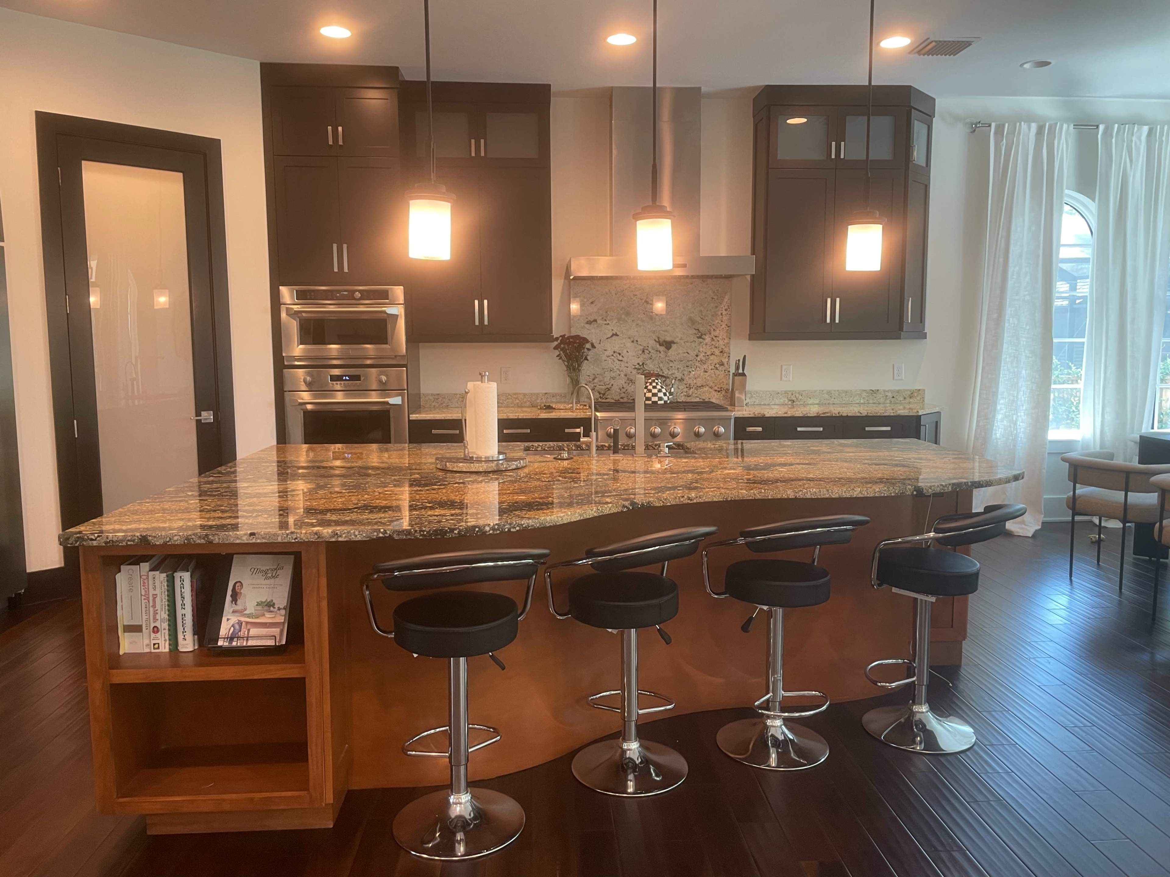 A modern kitchen featuring dark cabinetry, a large granite island with bar stools, and stainless steel appliances.