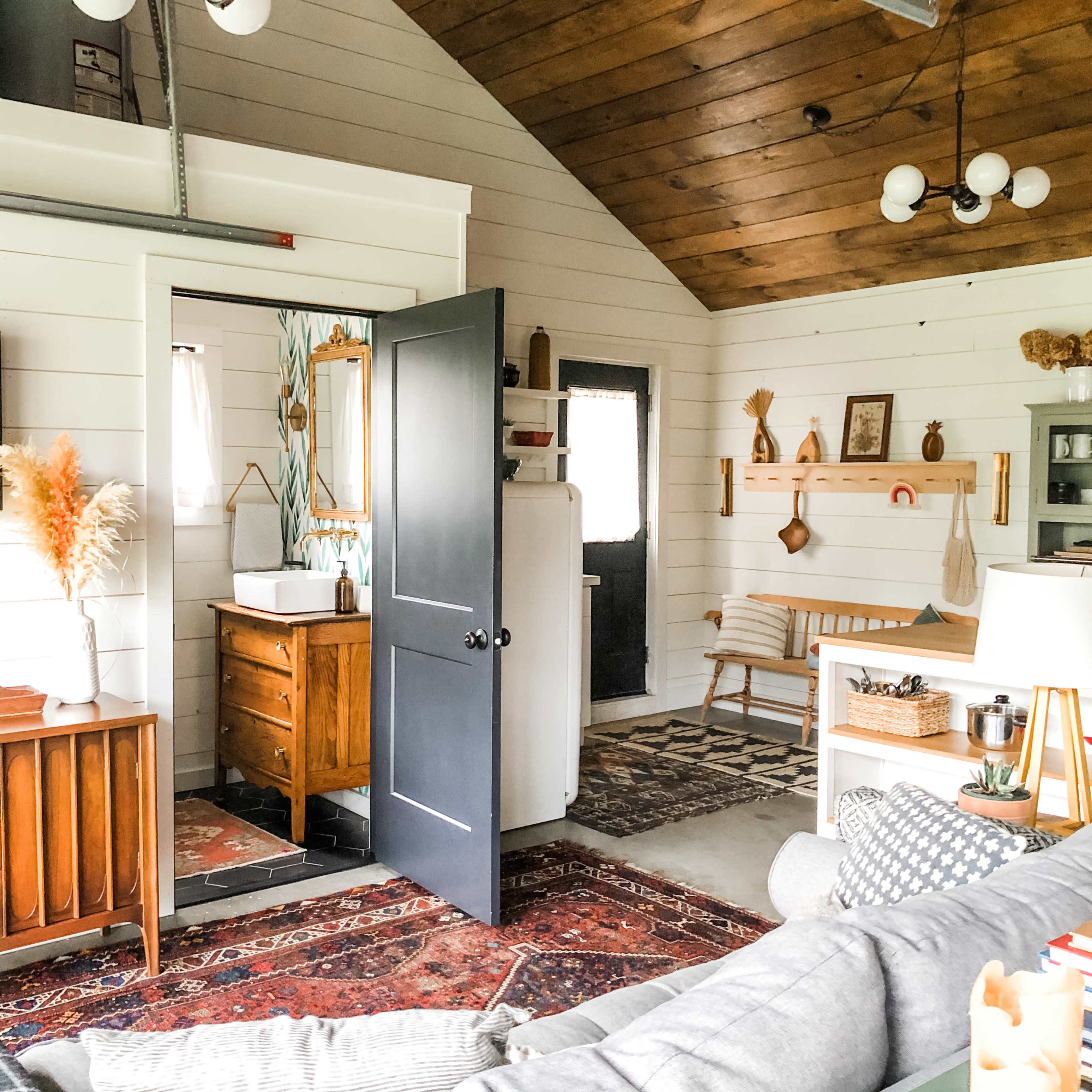 A cozy interior of a rustic-style living space with a visible bathroom area, wooden accents, and patterned rugs.