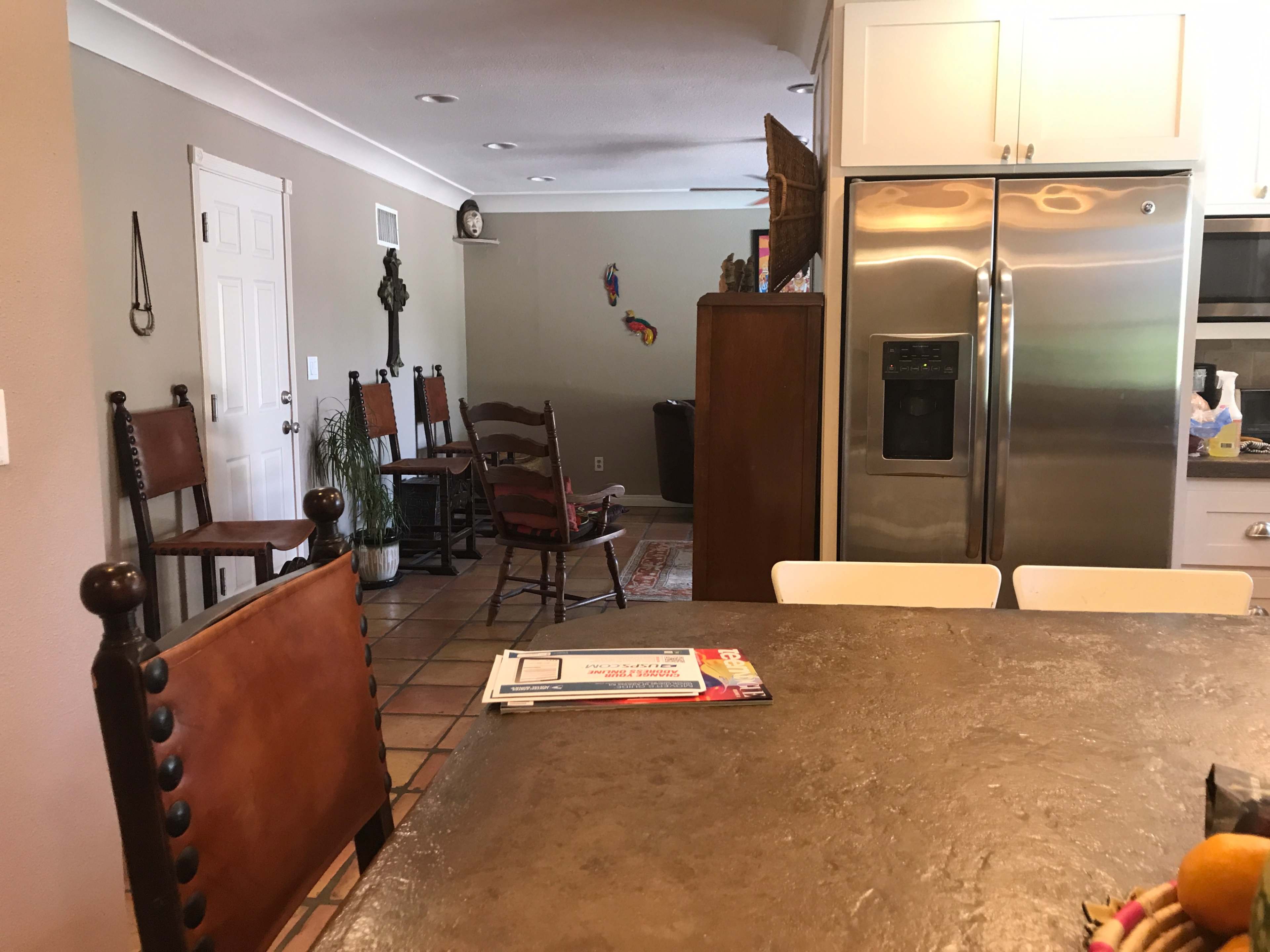 A kitchen area with a table in the foreground and chairs arranged in a living space visible in the background.