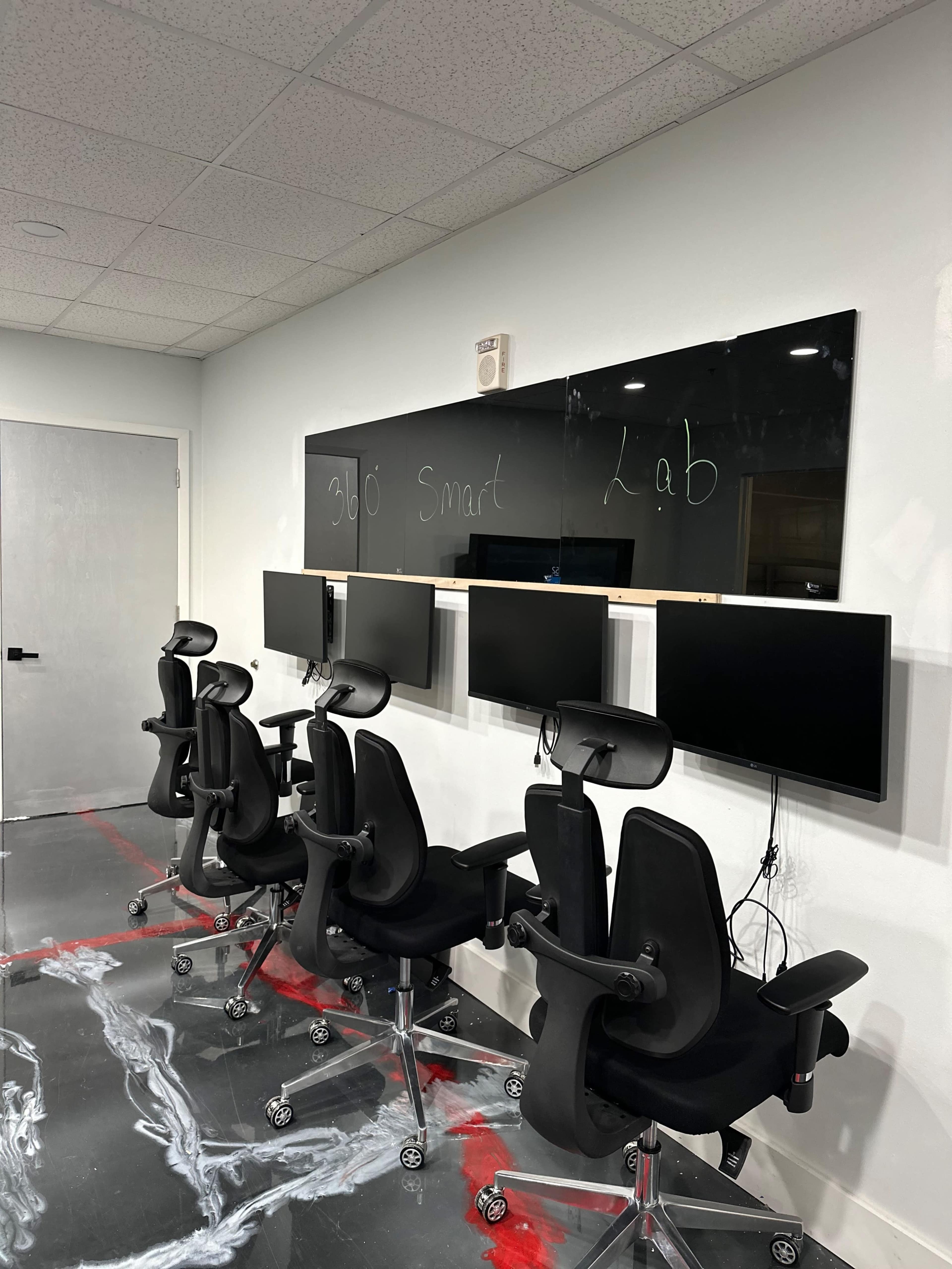 The image shows a row of black office chairs facing multiple computer monitors mounted on a wall in a room labeled "Smart Lab."