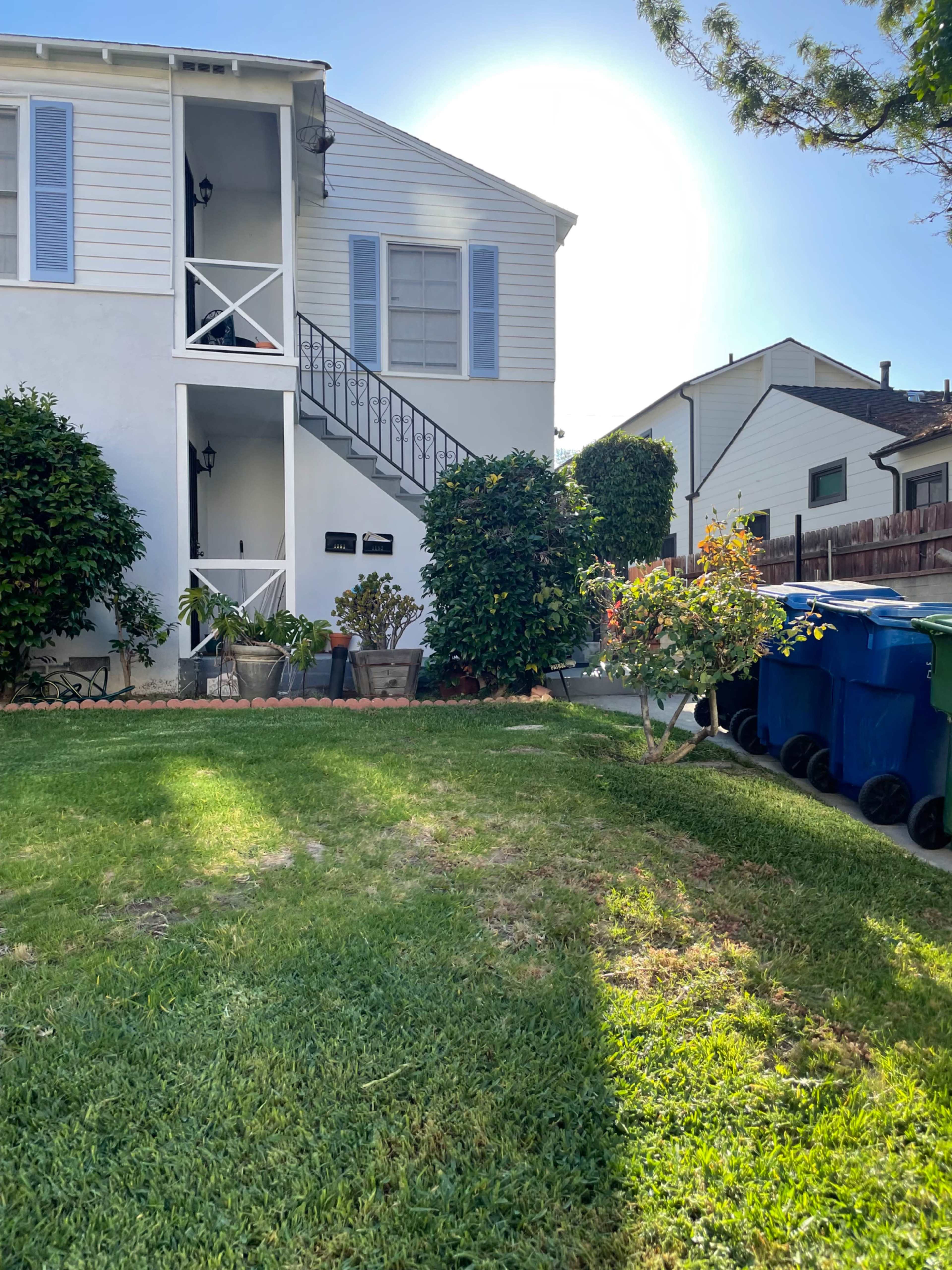 A two-story residential building with a staircase, potted plants, and several trash bins on the side.