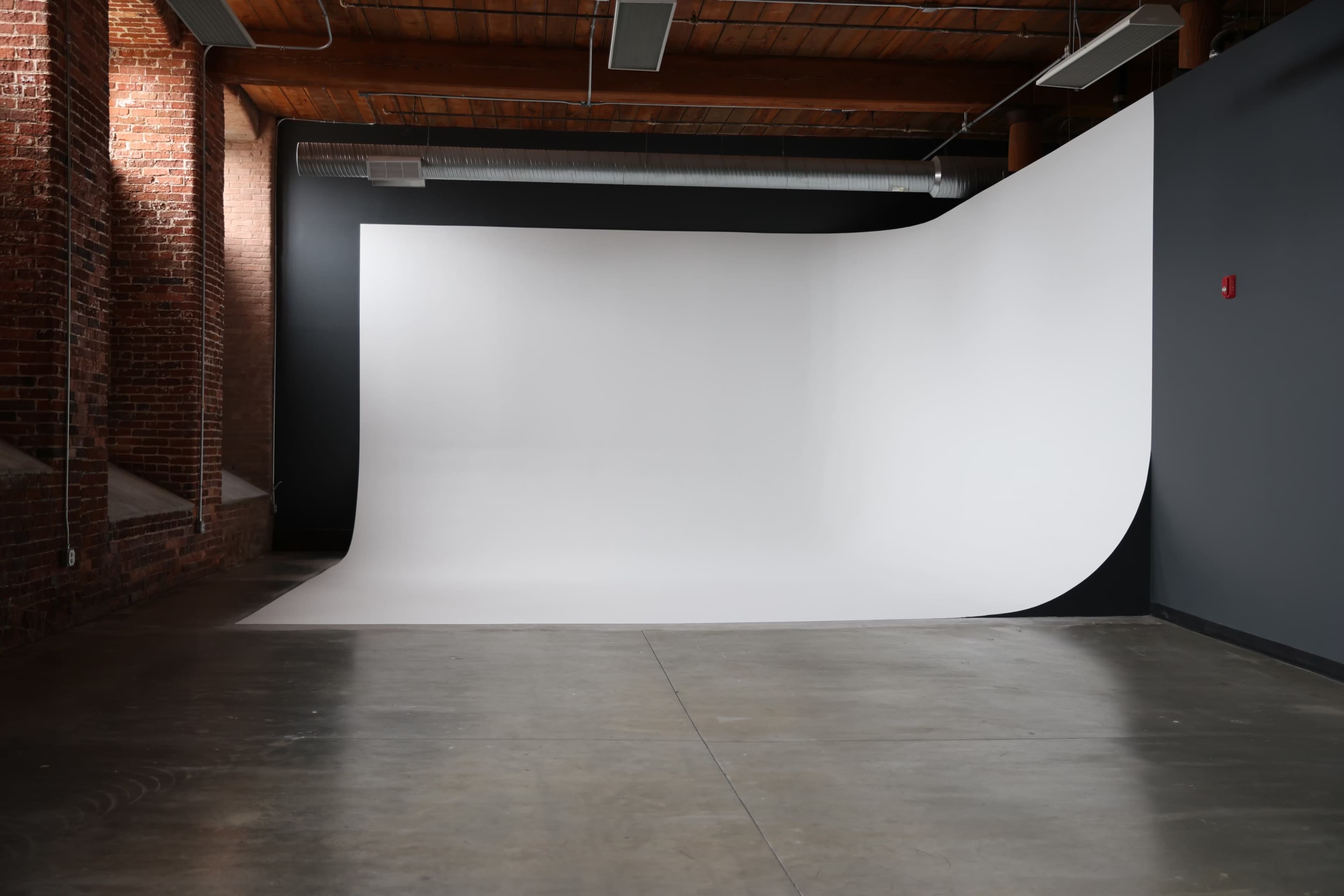 The image shows a spacious photography studio with a smooth white backdrop and exposed brick walls.