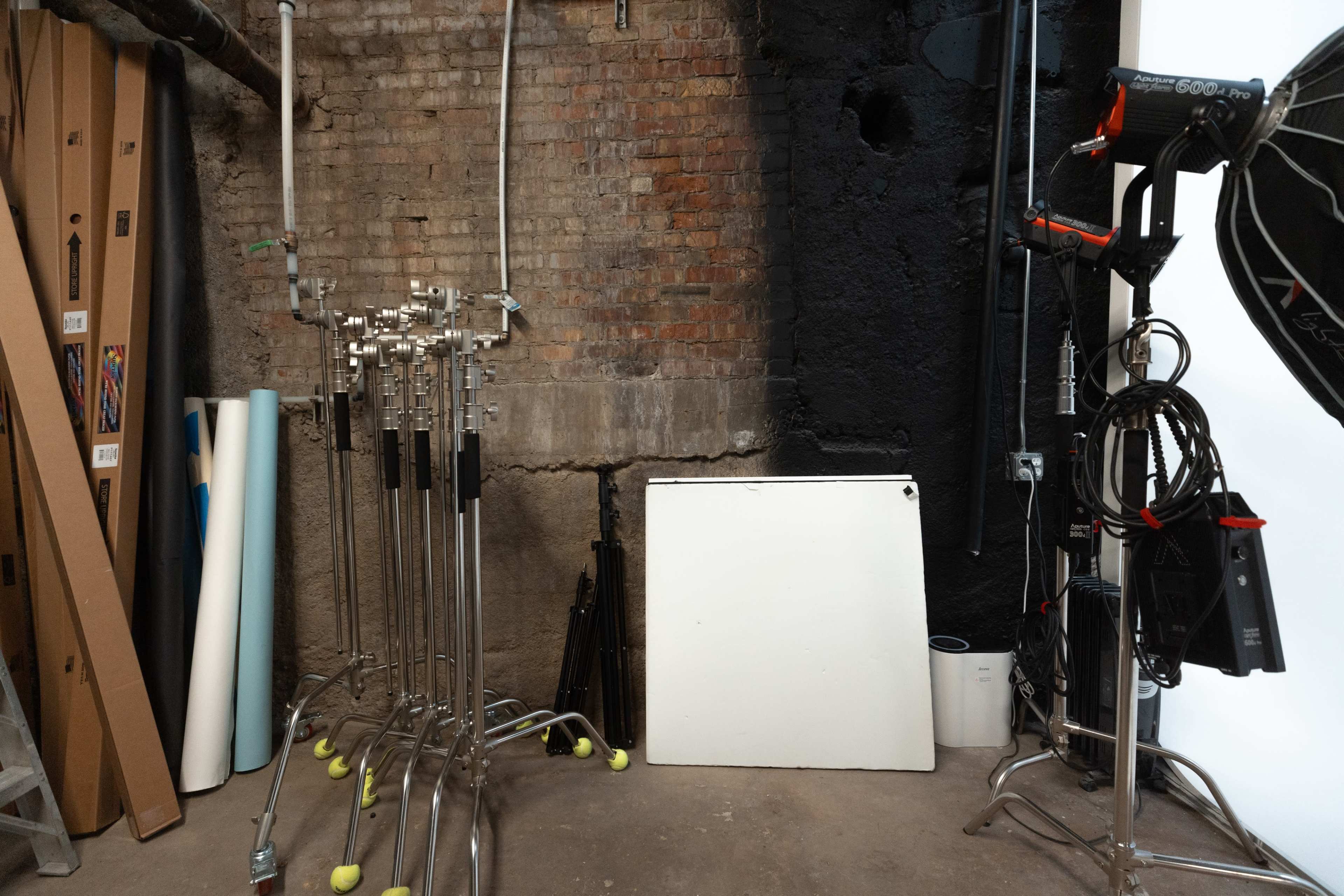 A storage area with various photography equipment, including stands, rolled-backdrops, and a white board.
