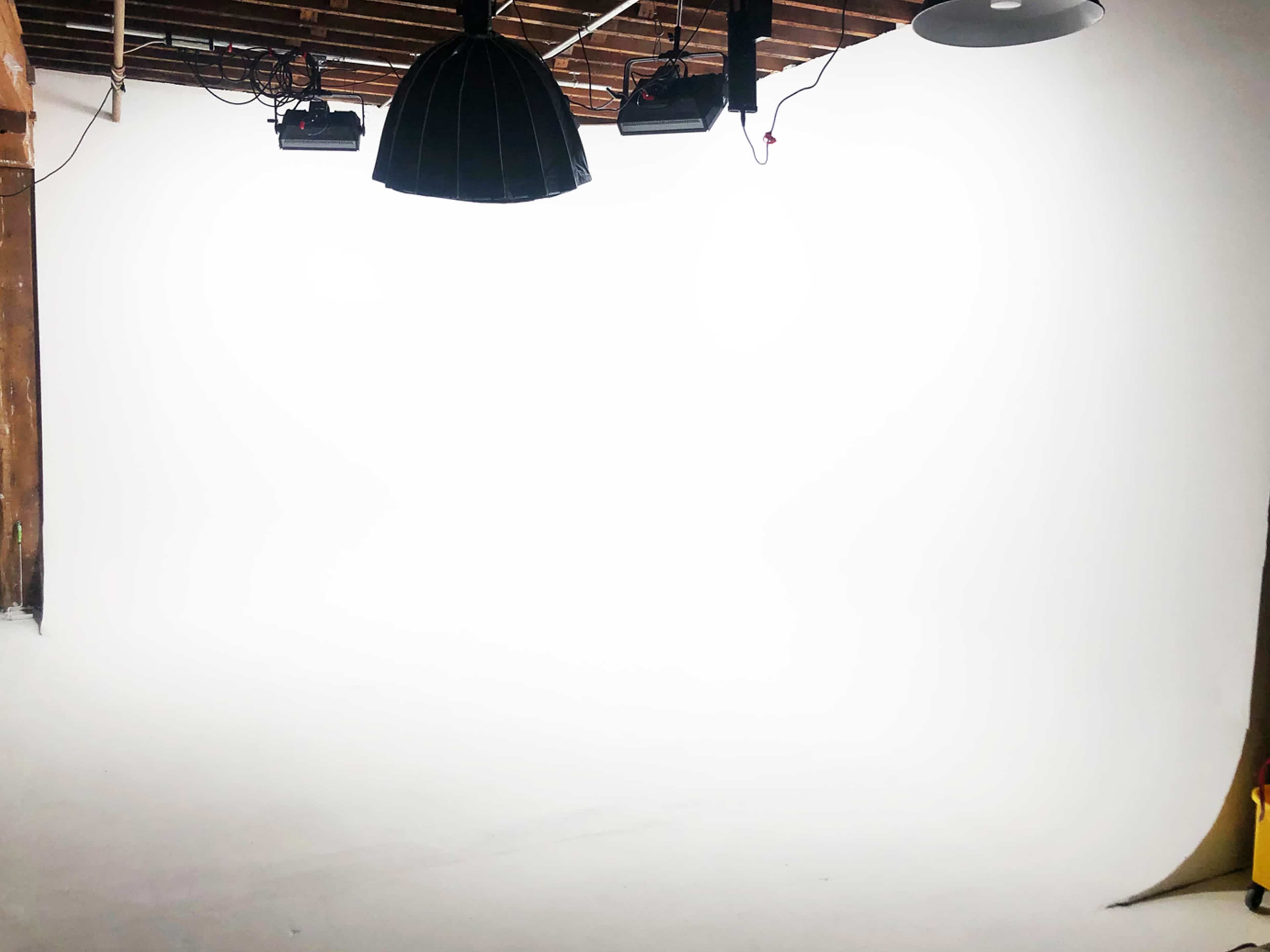 A spacious photography studio features a white backdrop, overhead lights, and exposed wooden beams.