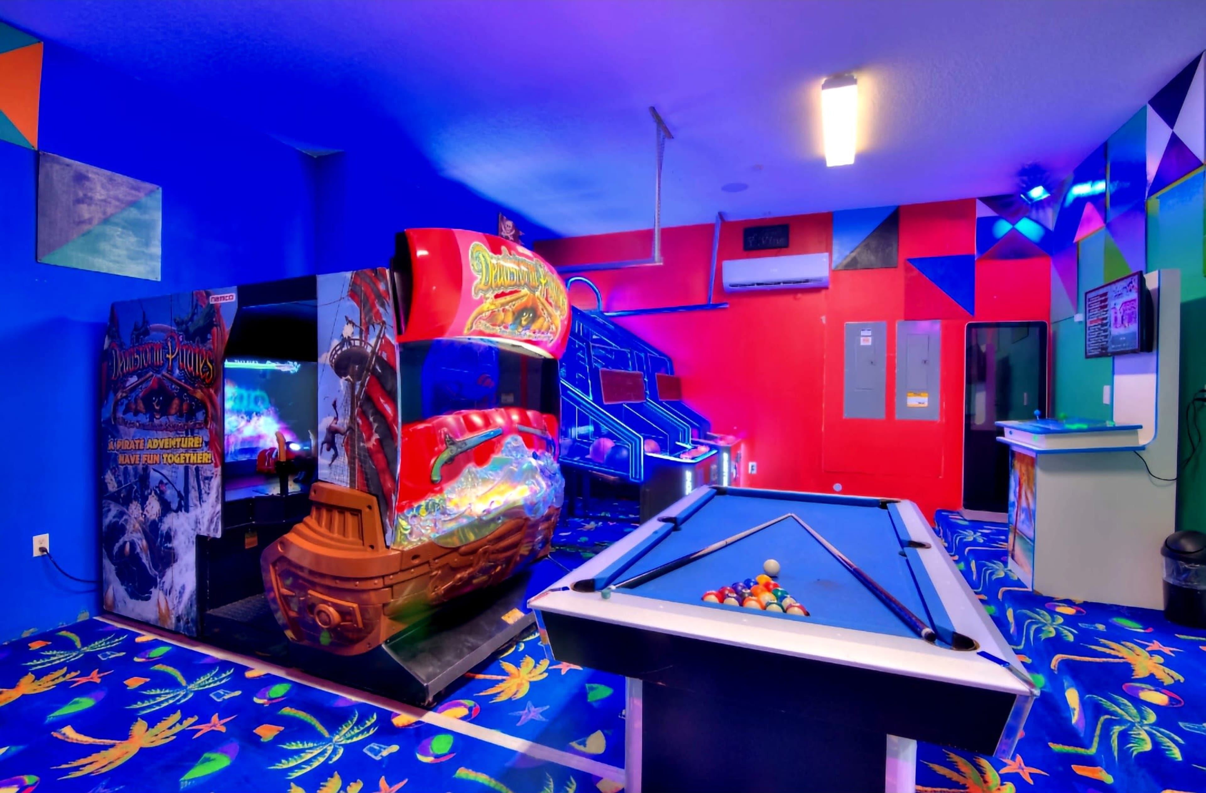 A vibrant arcade room featuring a pirate-themed arcade game and a pool table on a colorful patterned carpet.