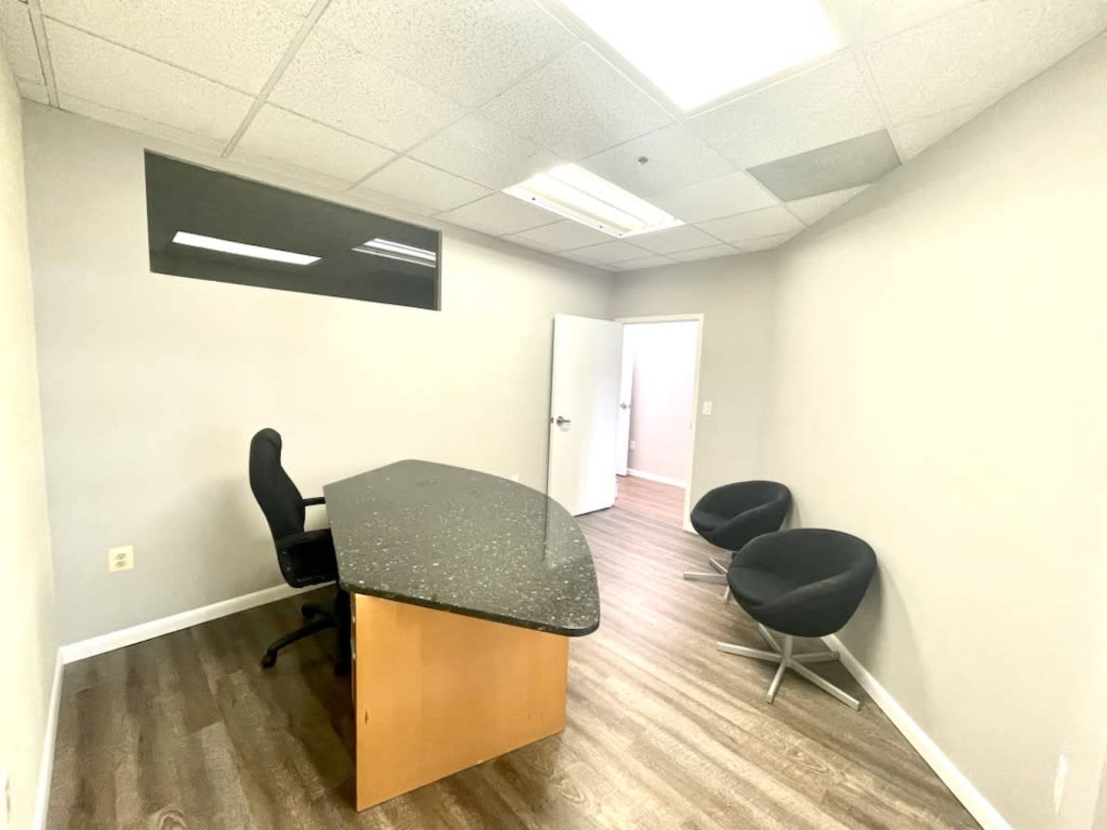 A minimalist office space featuring a black granite desk, an office chair, and two circular black chairs.