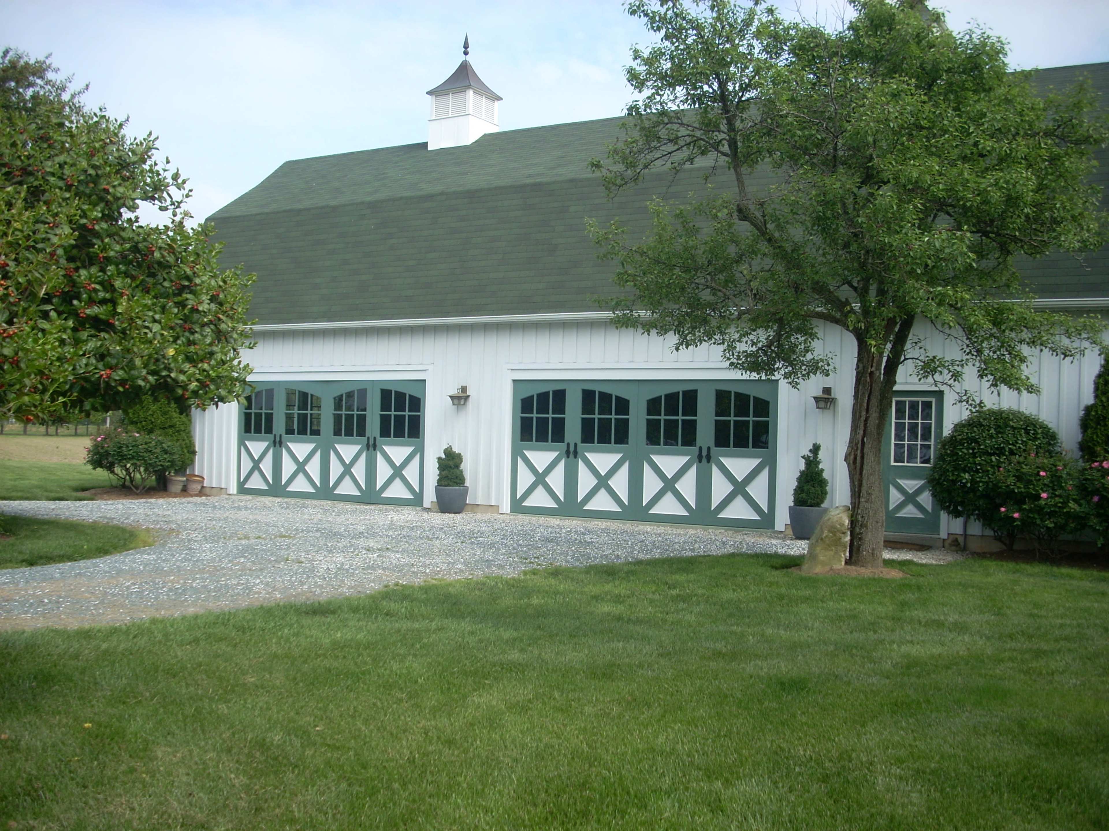 A white barn-style building with green accents, featuring large garage doors and a landscaped yard.