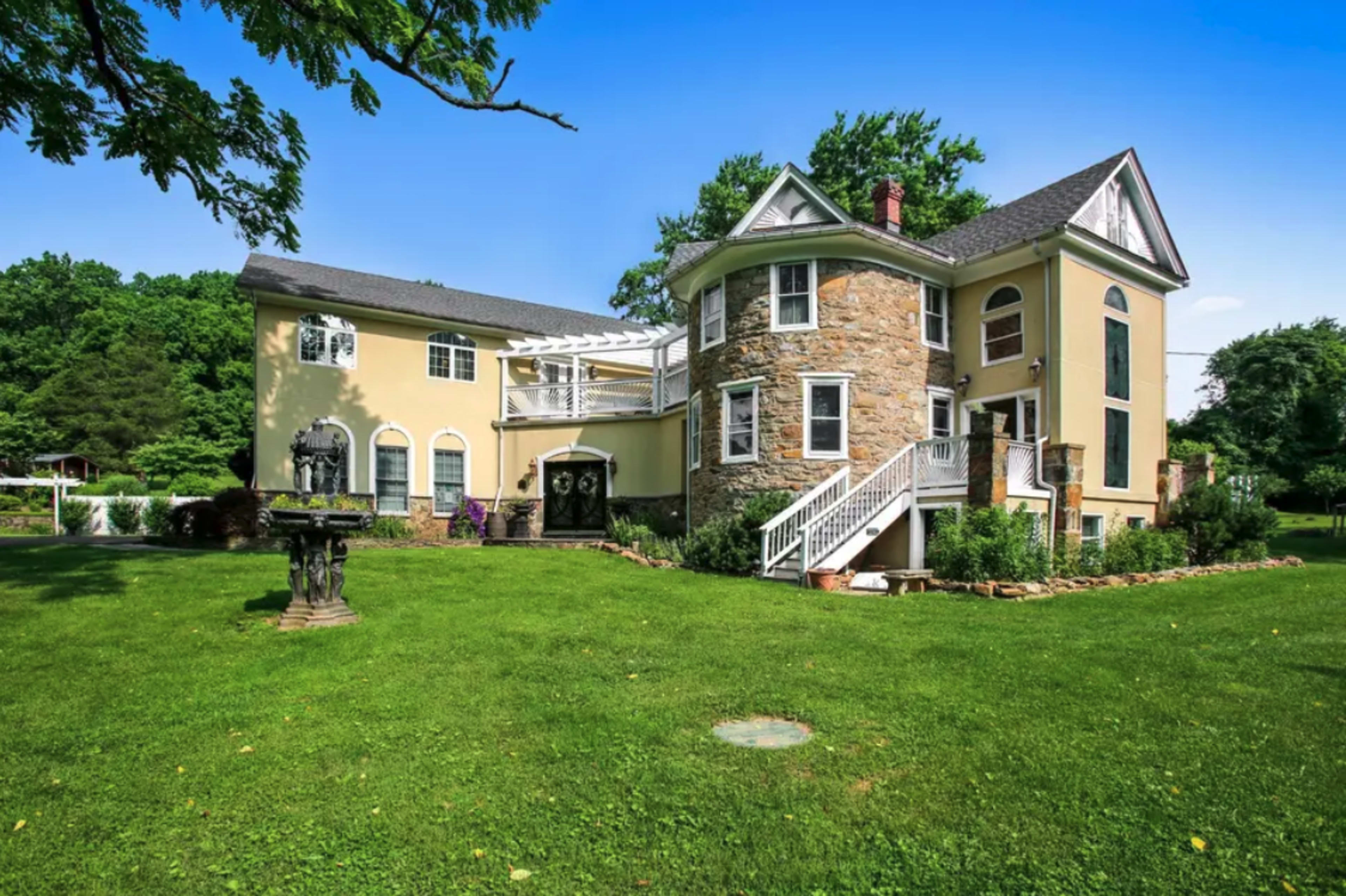 A large two-story house features a stone turret, a wraparound porch, and a landscaped yard.