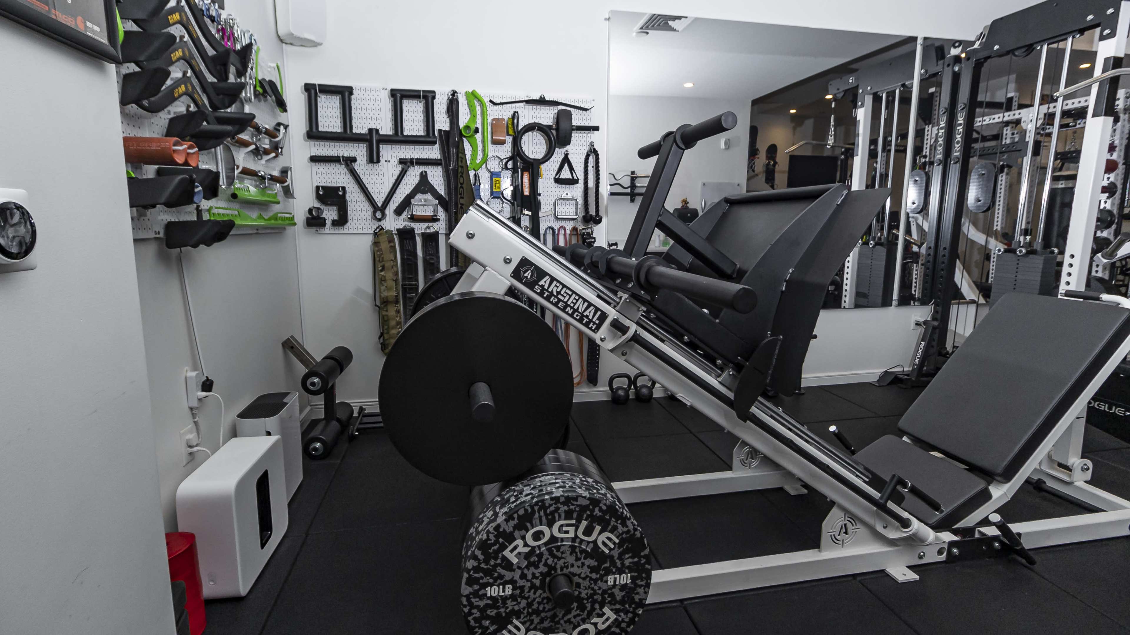 A well-equipped home gym featuring a leg press machine, weight plates, and various exercise equipment mounted on the wall.
