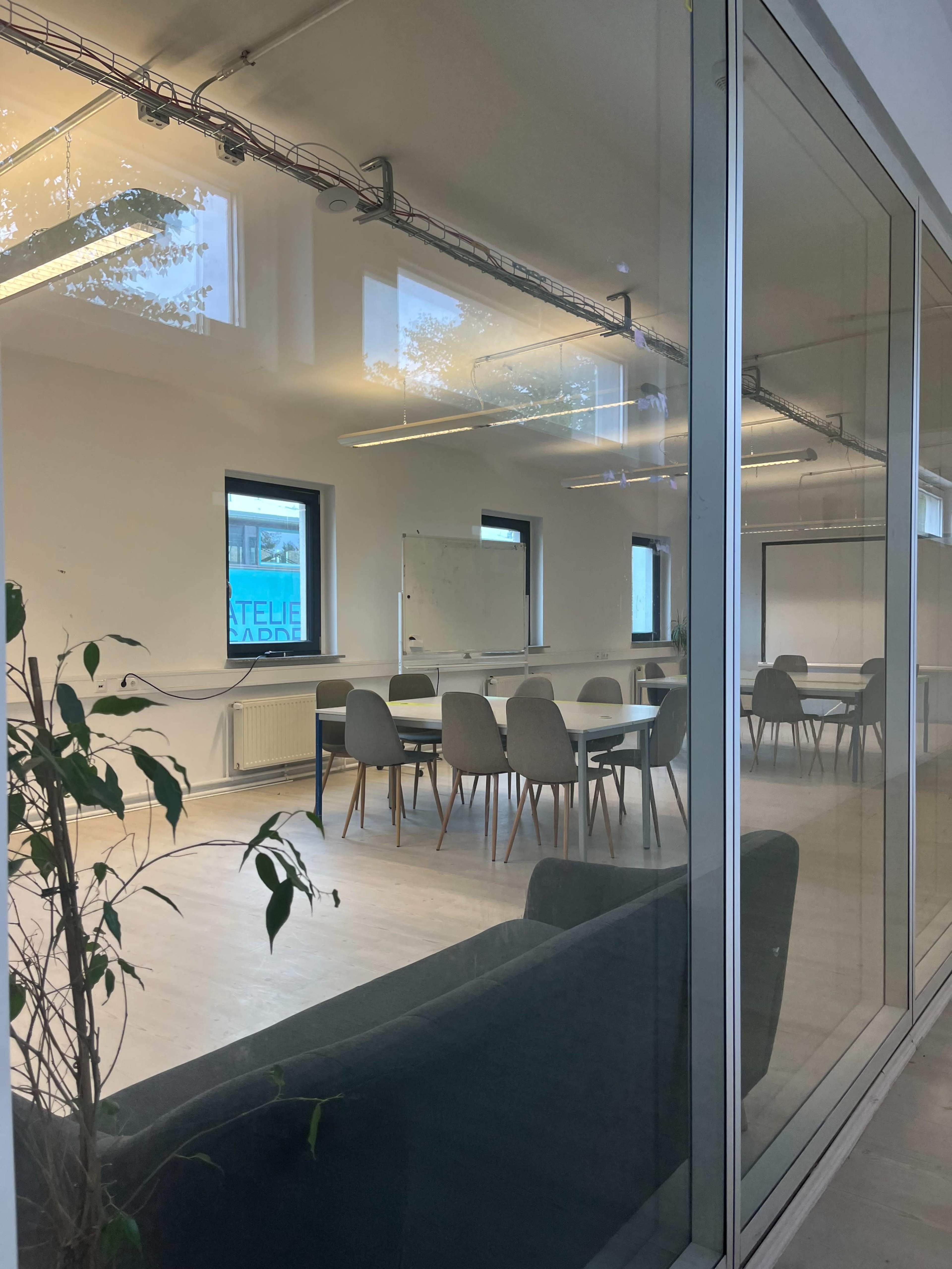 The image shows a modern conference room visible through a glass wall, featuring a large table surrounded by several chairs and a whiteboard.