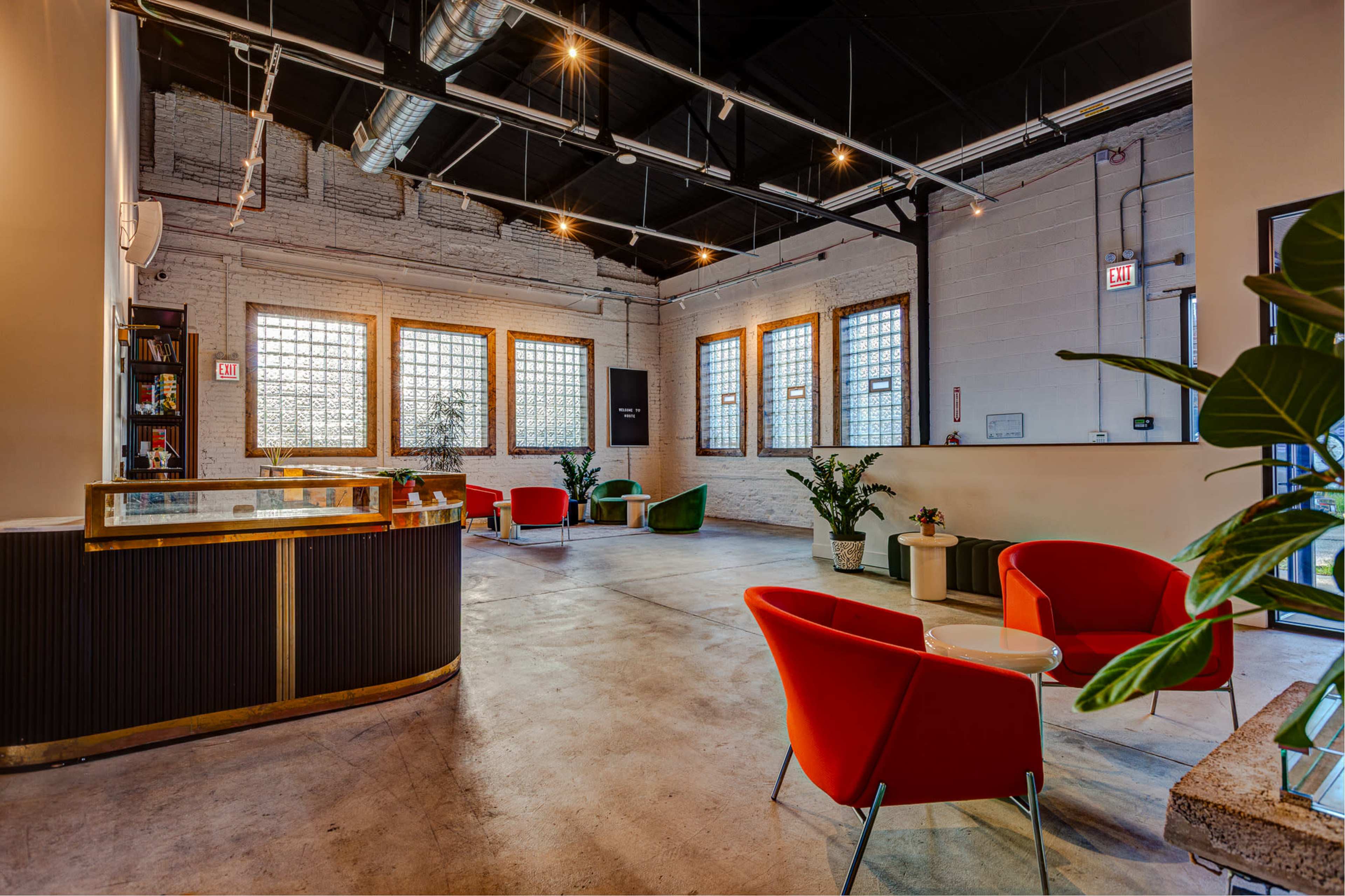 The image shows a modern, spacious interior of a lounge area with large windows, colorful seating, and a reception desk.