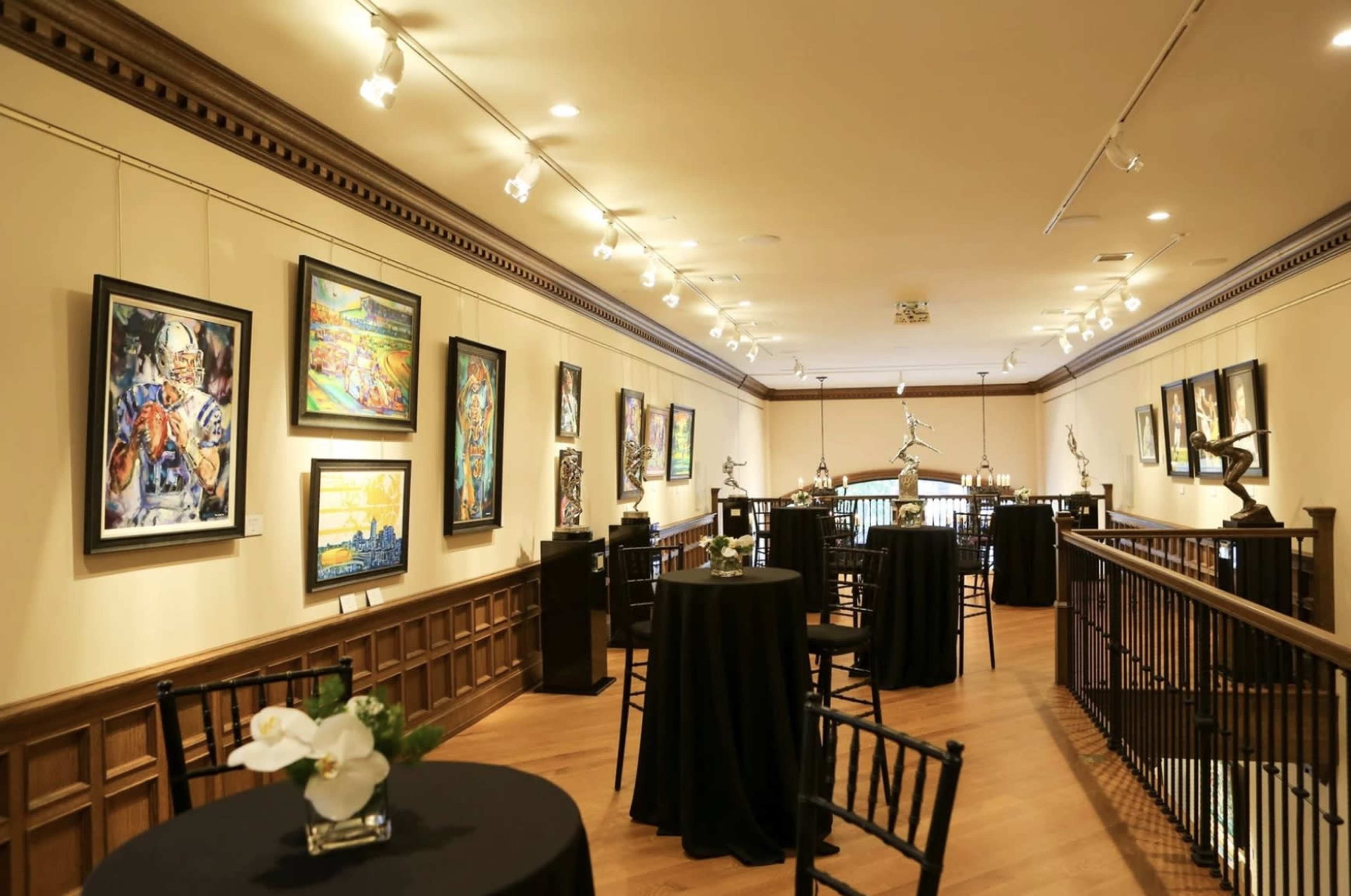 An art gallery featuring a long hallway with framed artworks on the walls and small tables positioned along the sides.