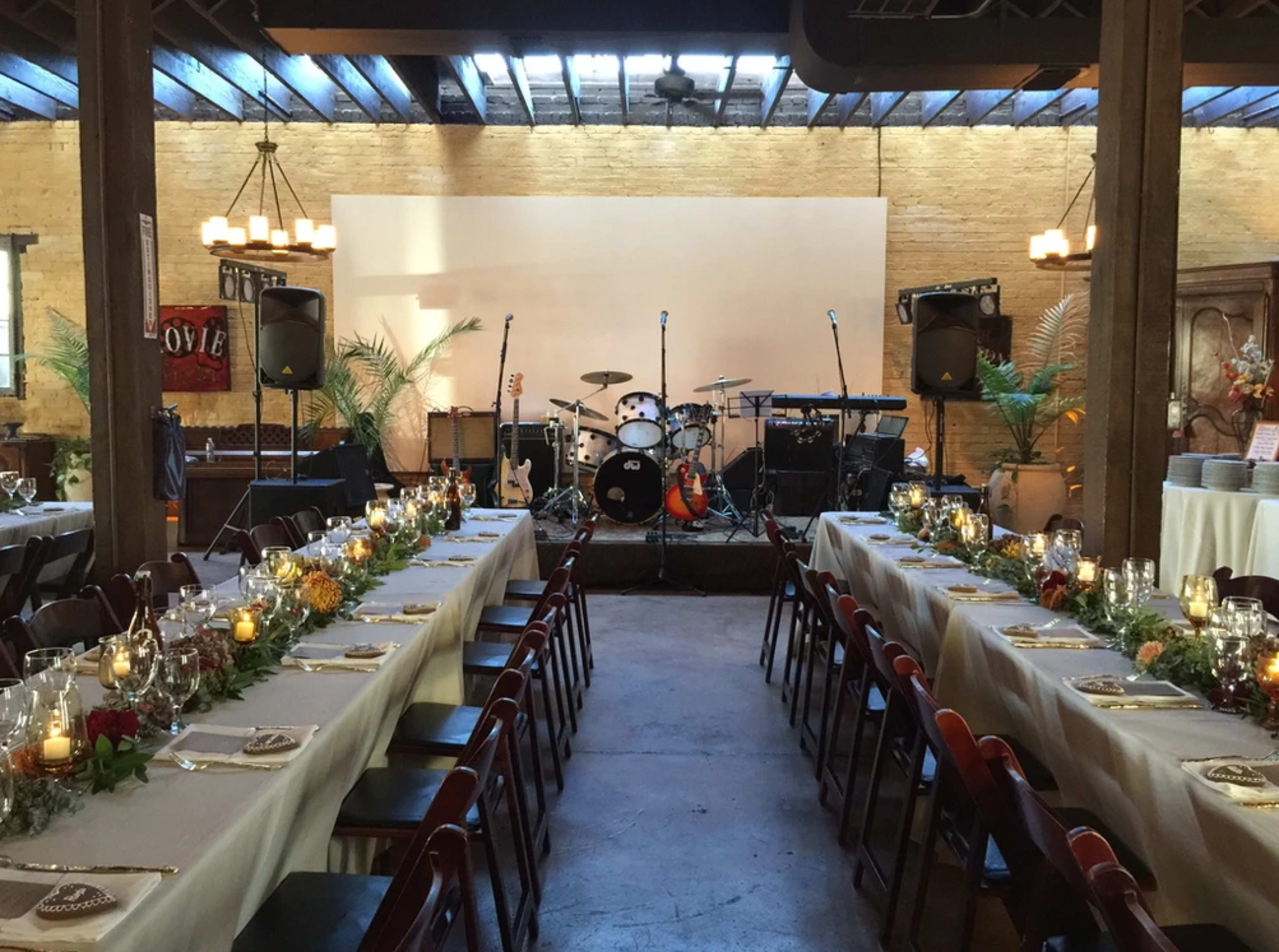 A dining area is set up for a wedding reception, featuring long tables with centerpieces and a stage equipped with musical instruments in the background.