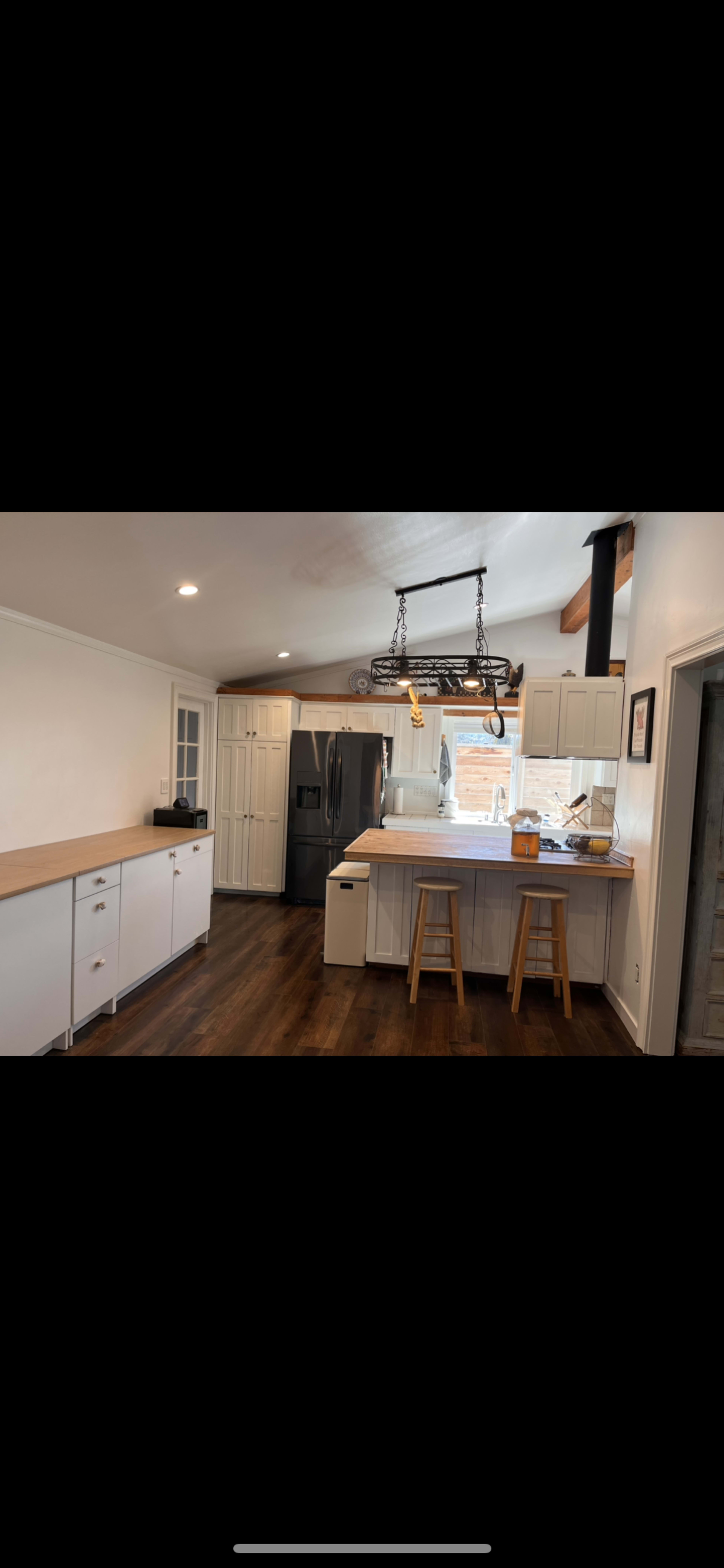 A modern kitchen with light-colored cabinetry, a wooden countertop, and two wooden stools near an island.