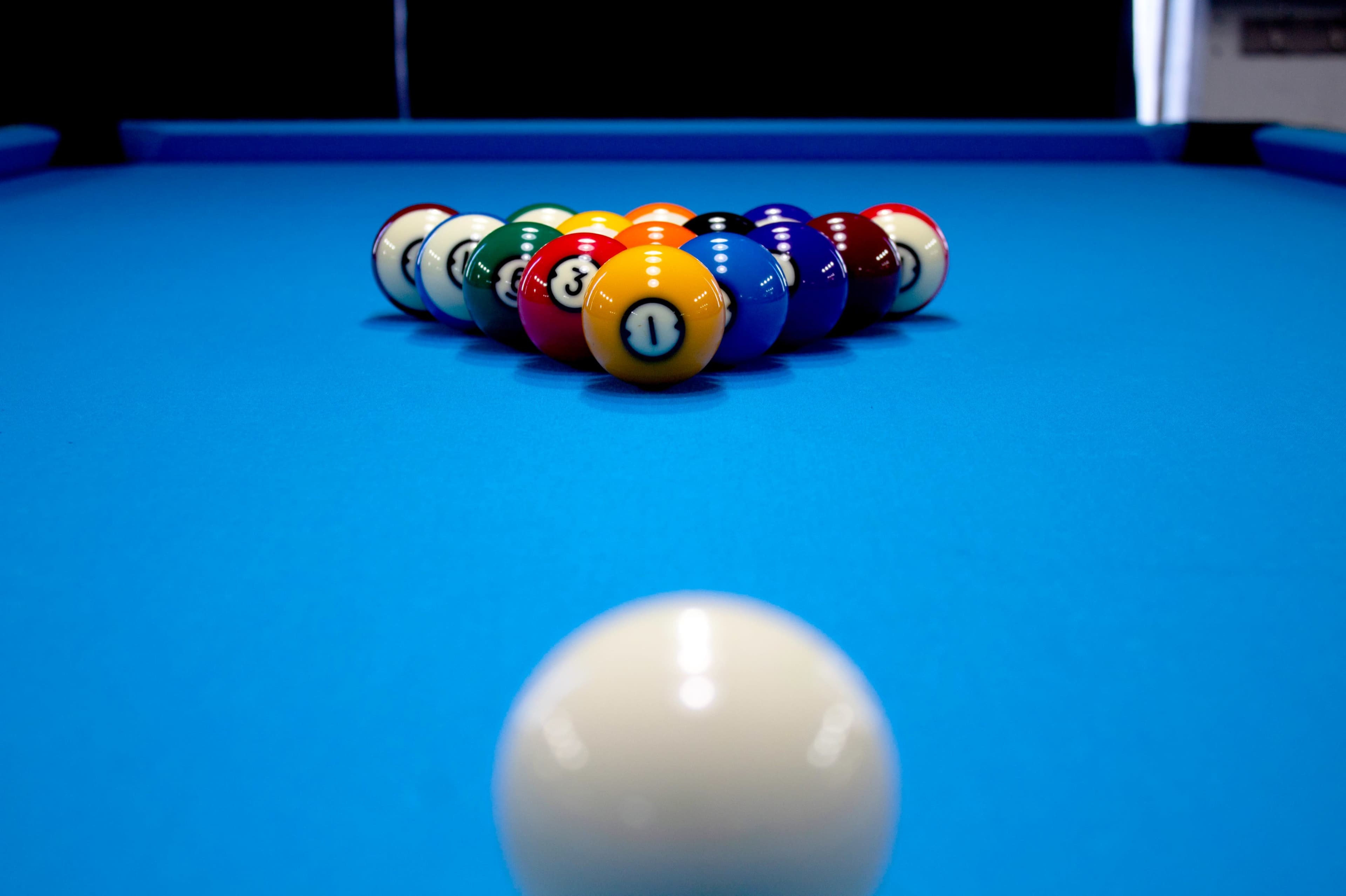 A cue ball is positioned in front of a rack of colorful billiard balls set up in a triangle on a blue felt pool table.