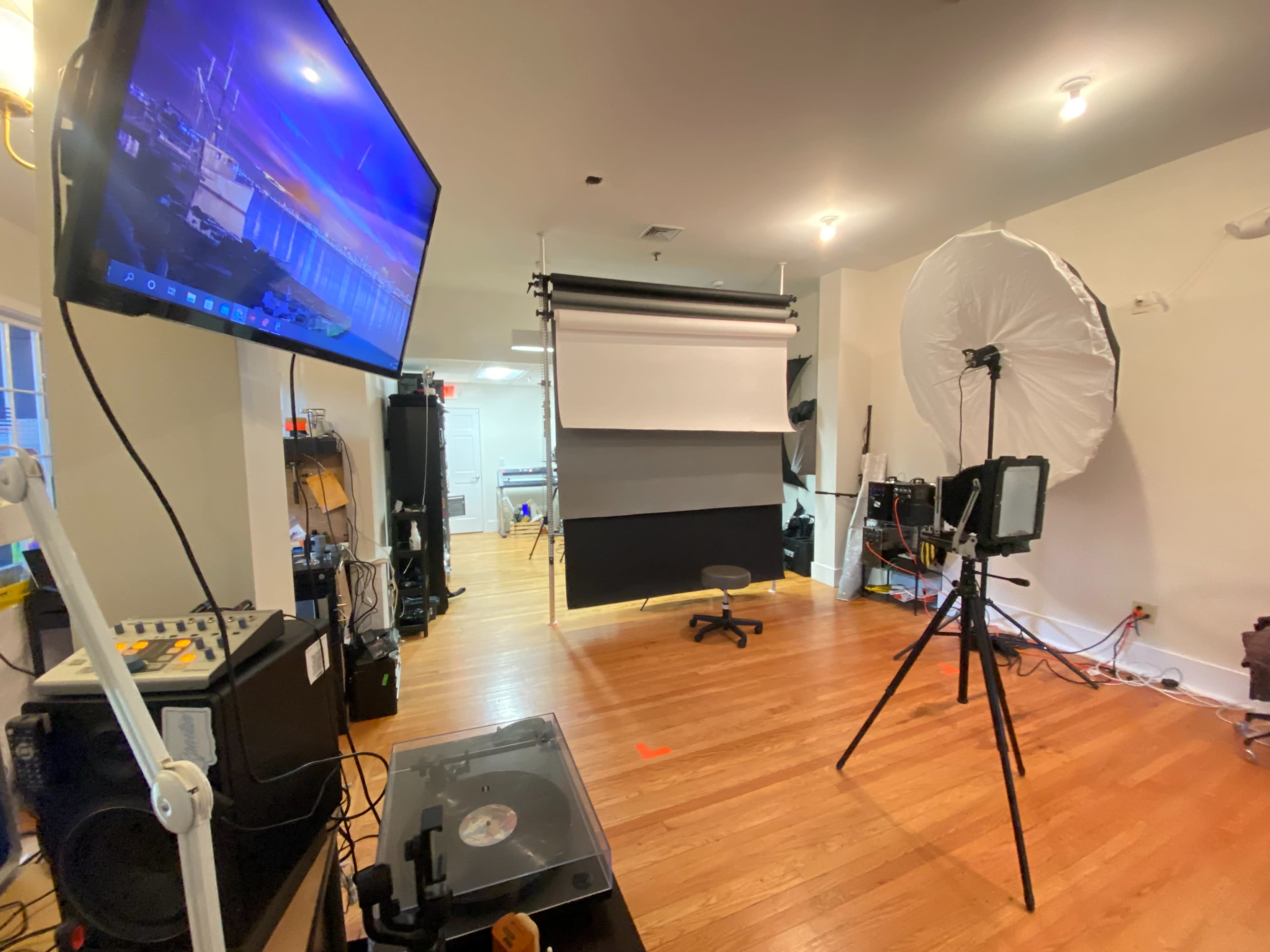 A photography studio is set up with a backdrop, lighting equipment, and a computer monitor displaying an image.