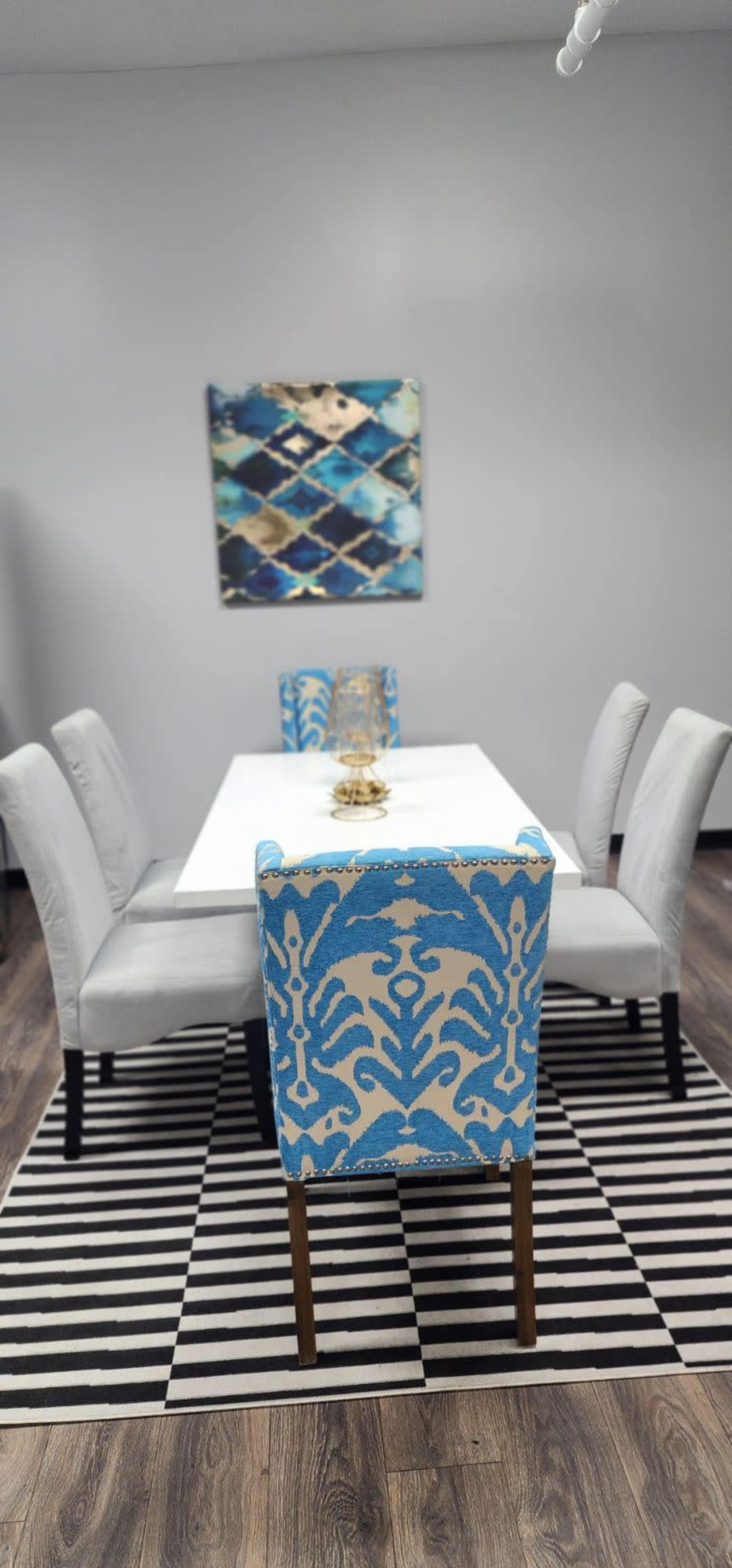 A dining area features a white table surrounded by patterned blue and white chairs, and a striped black and white rug underneath.