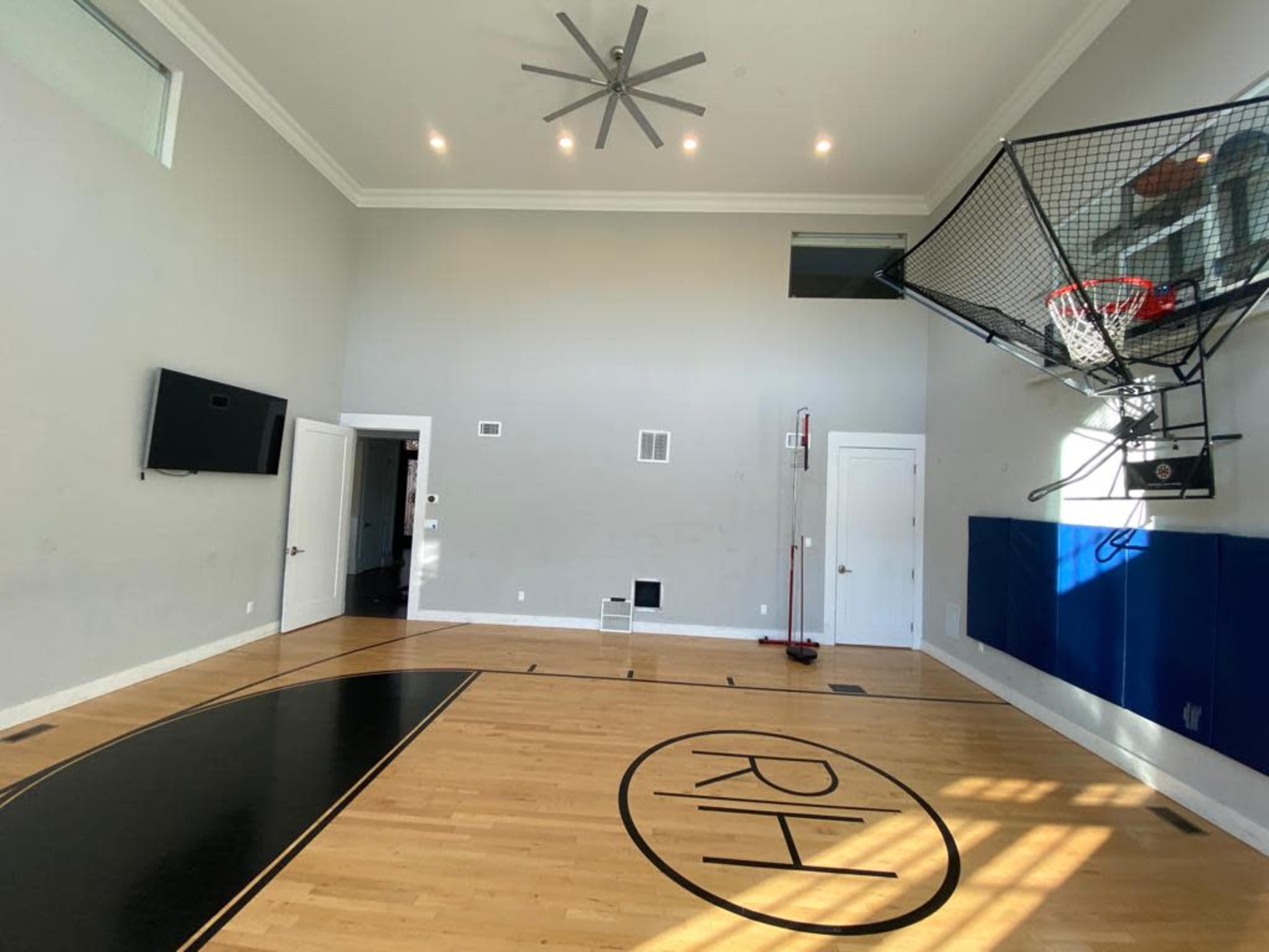 The image shows an indoor basketball court with a hoop mounted on the wall and a court marking featuring the initials "RH."
