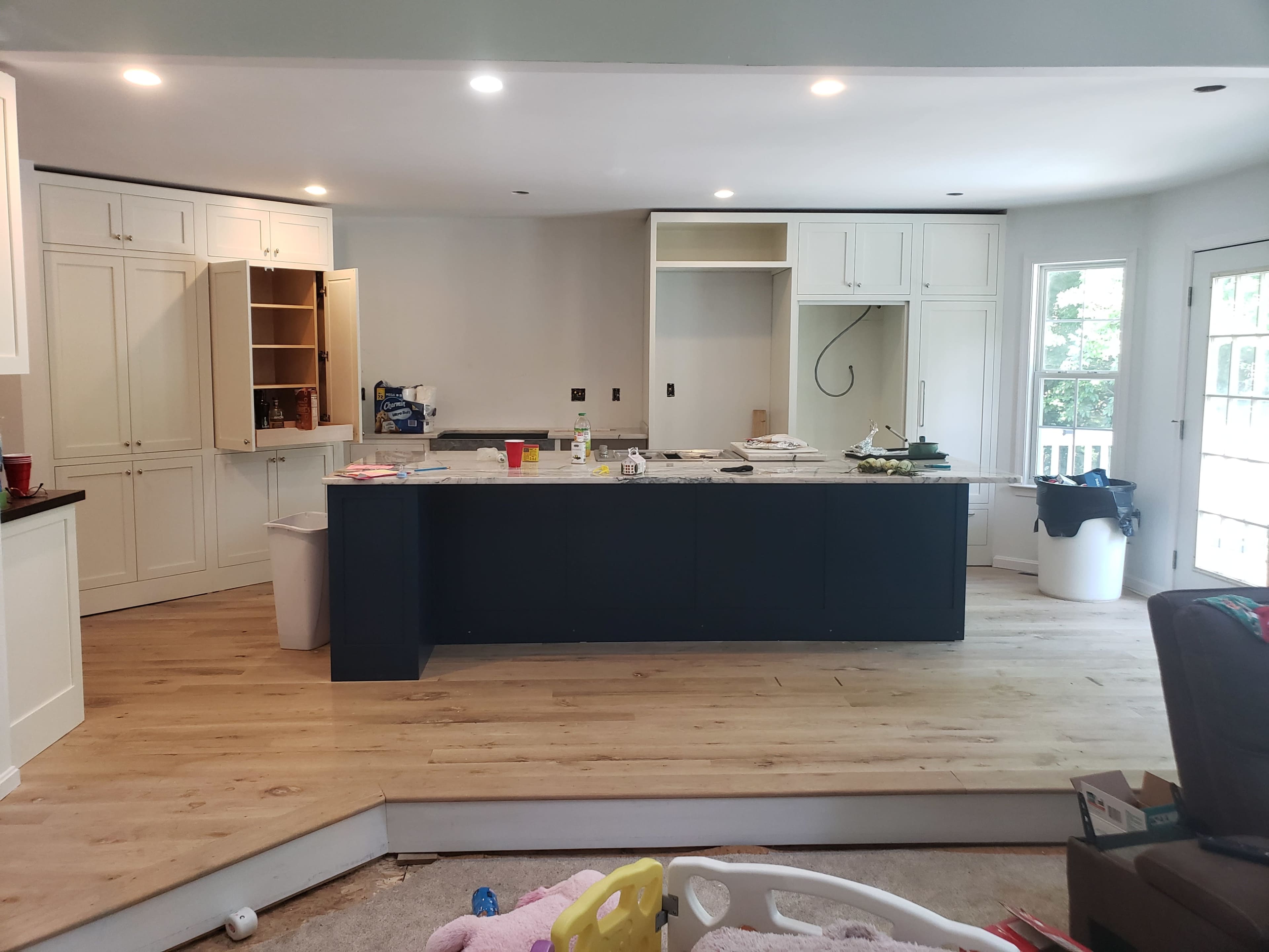 The image shows a spacious kitchen with an island, wooden flooring, and unfinished cabinetry.