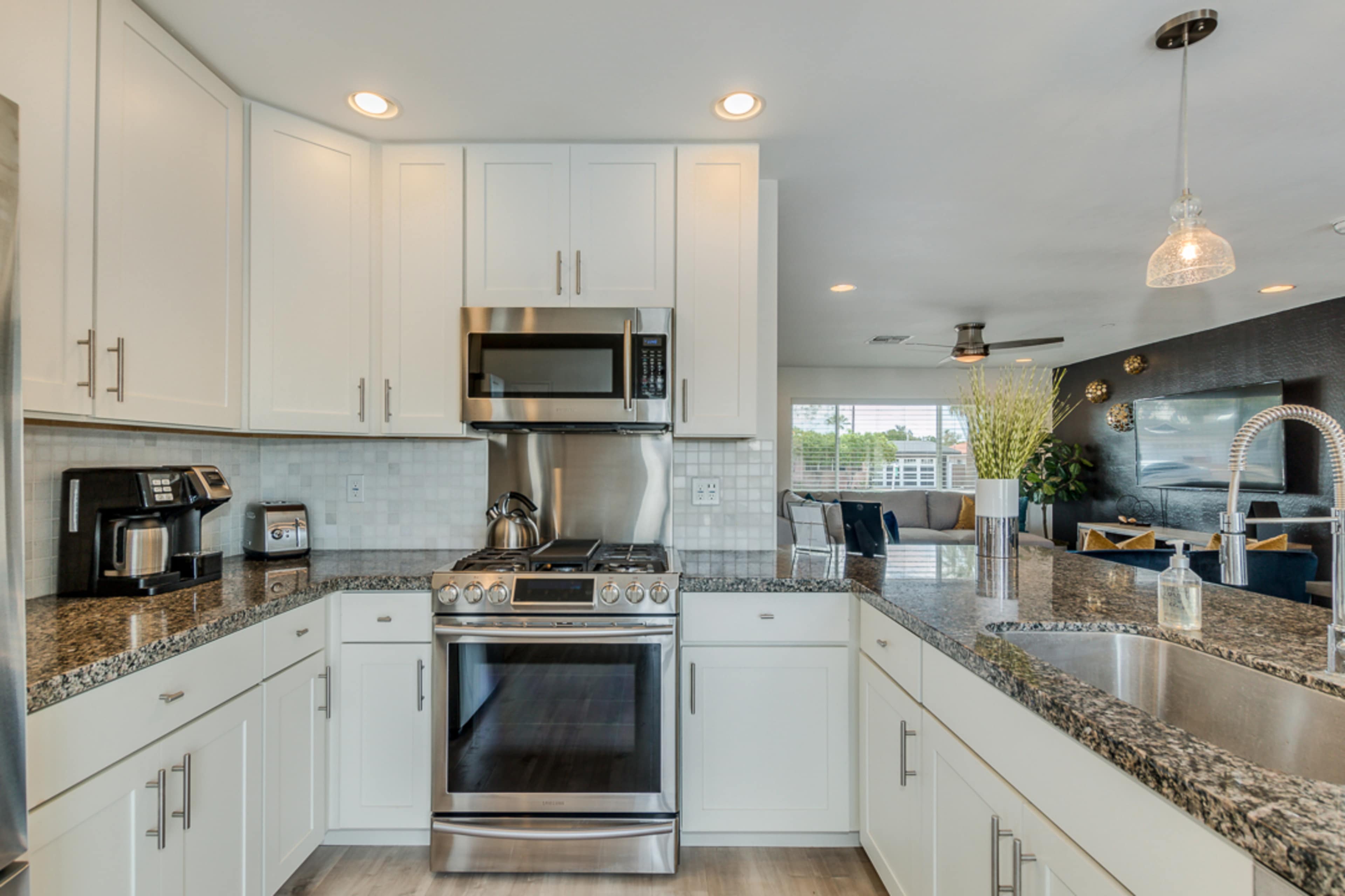 A modern kitchen features stainless steel appliances, white cabinetry, and granite countertops, with an open layout connecting to a living area.