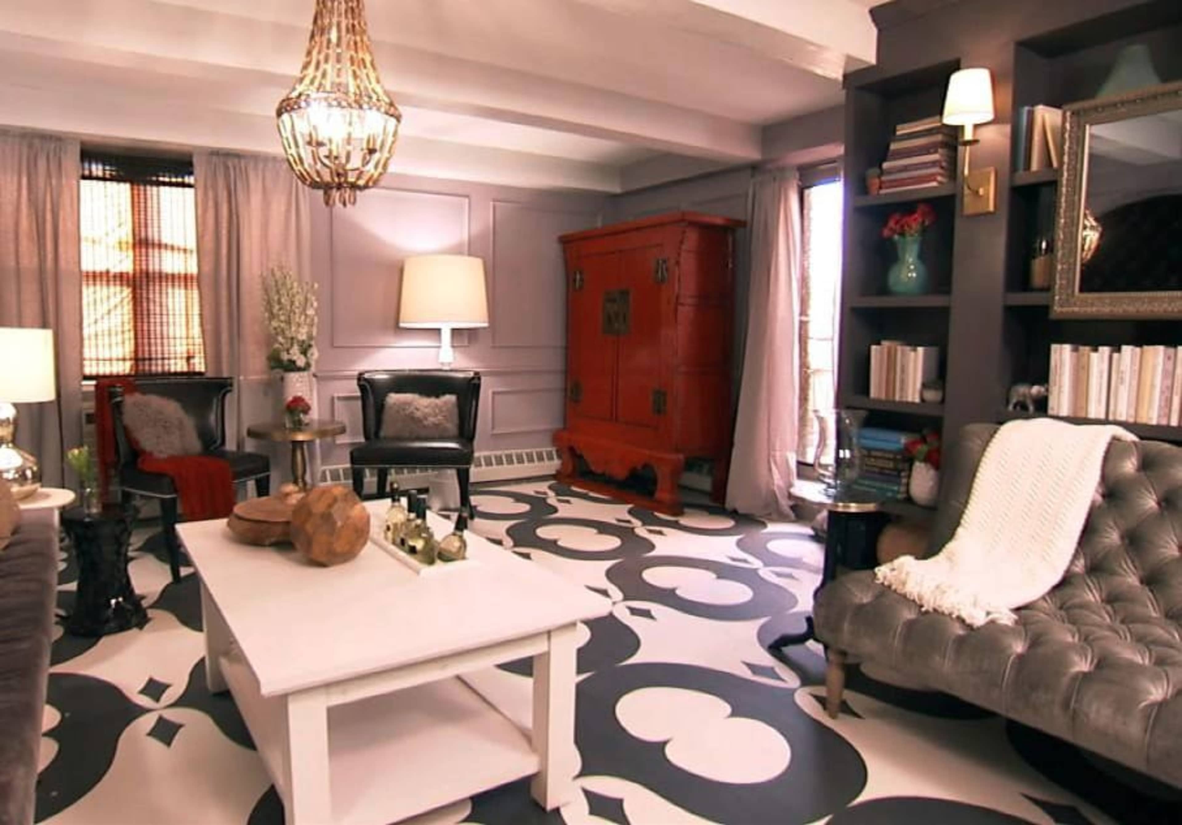 The living room features a gray tufted sofa, a white coffee table, and a vibrant red cabinet against a patterned floor.