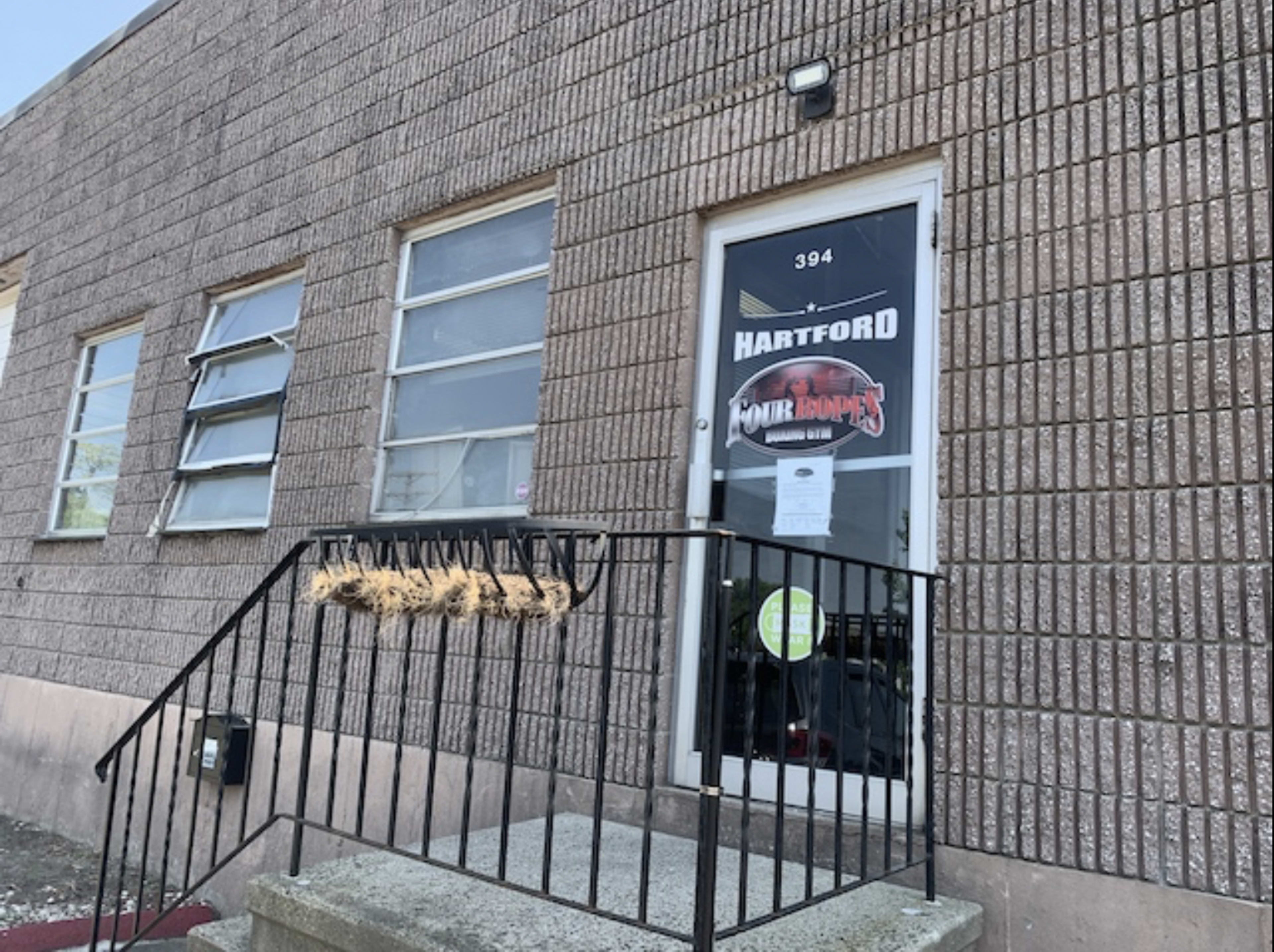 The image shows a concrete building entrance with a glass door displaying a sign that reads "Hartford Four Hops" and a set of stairs leading up to it.