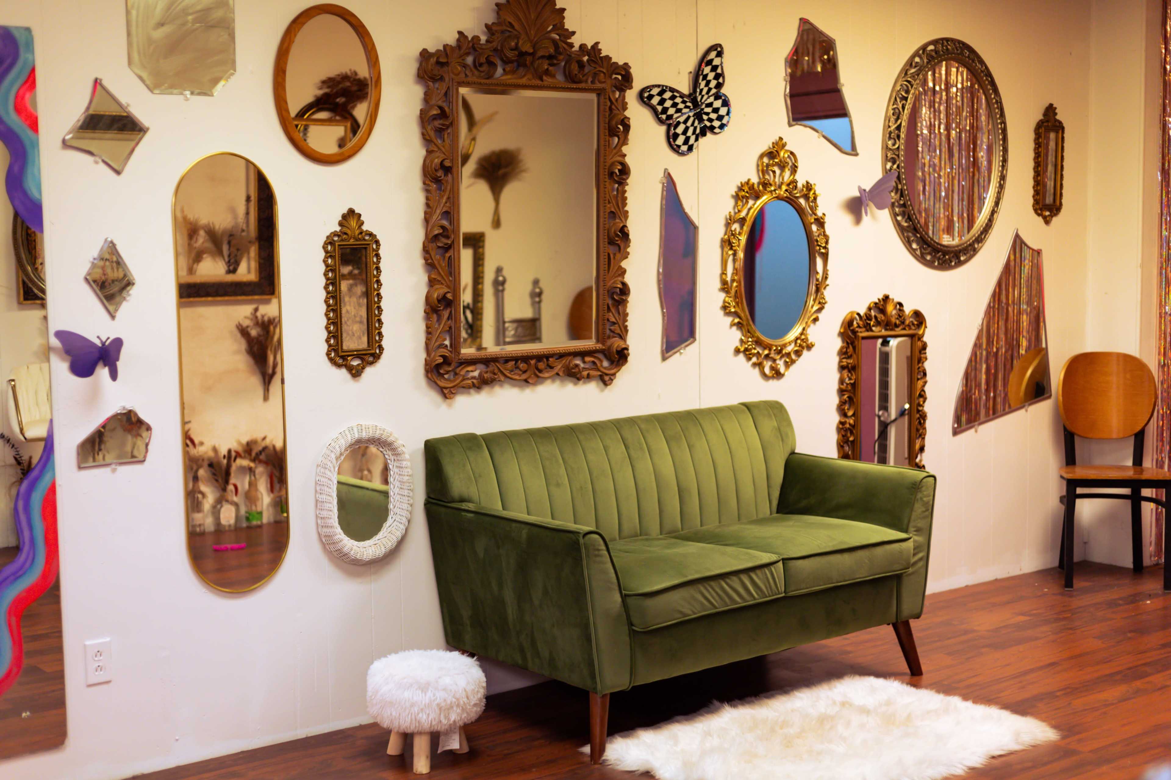 A green velvet couch positioned next to a wall adorned with various mirrors, frames, and decorative objects.