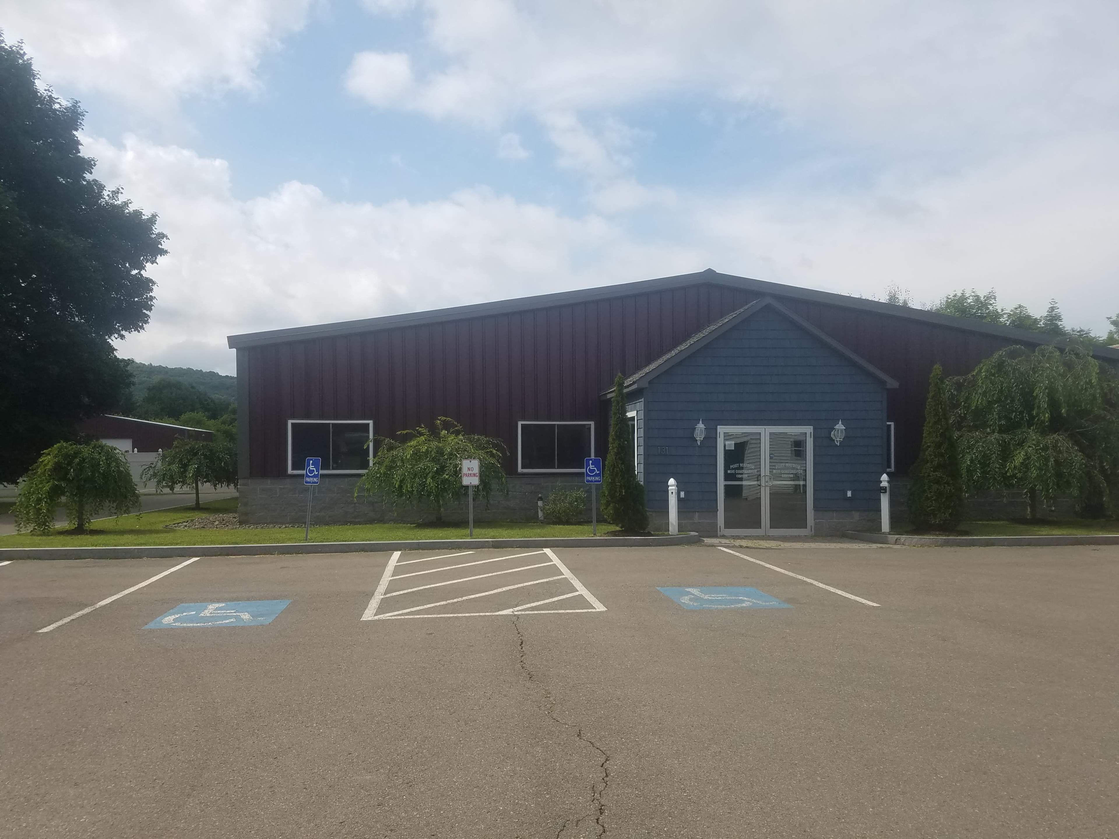 A large, blue and maroon building with accessible parking spaces and landscaped greenery in front.