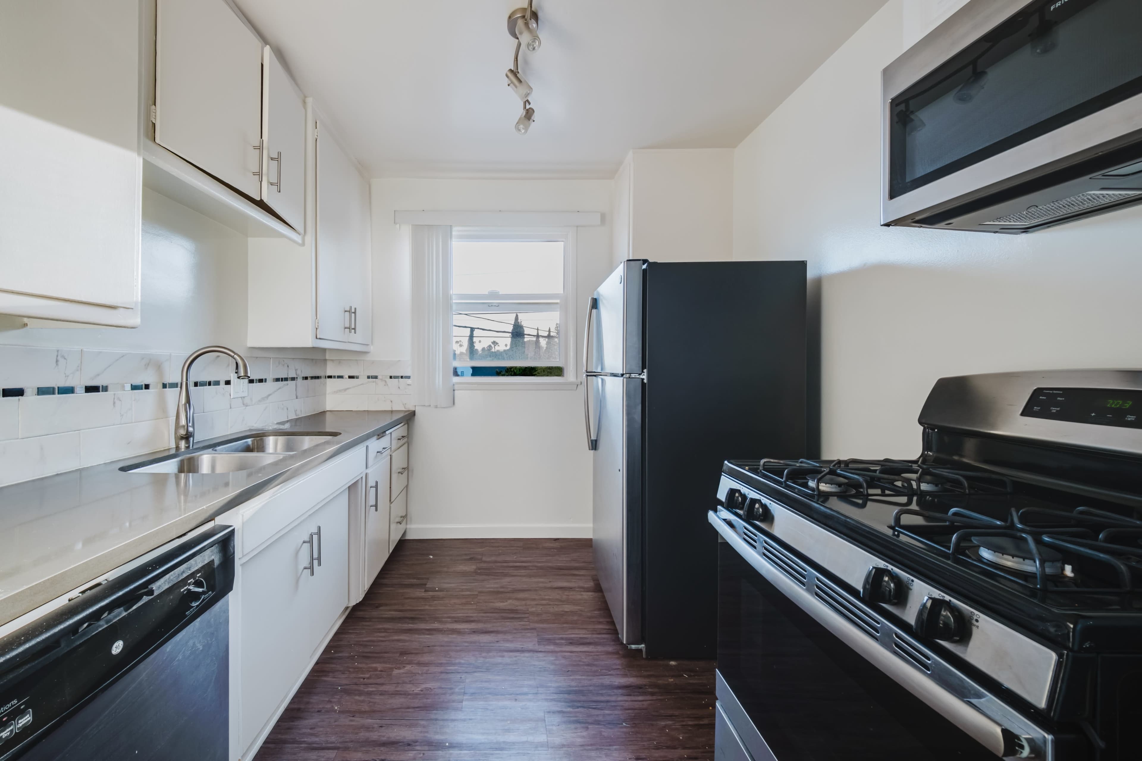 The image shows a clean kitchen featuring white cabinets, a stainless steel sink, a black refrigerator, and a gas stove.