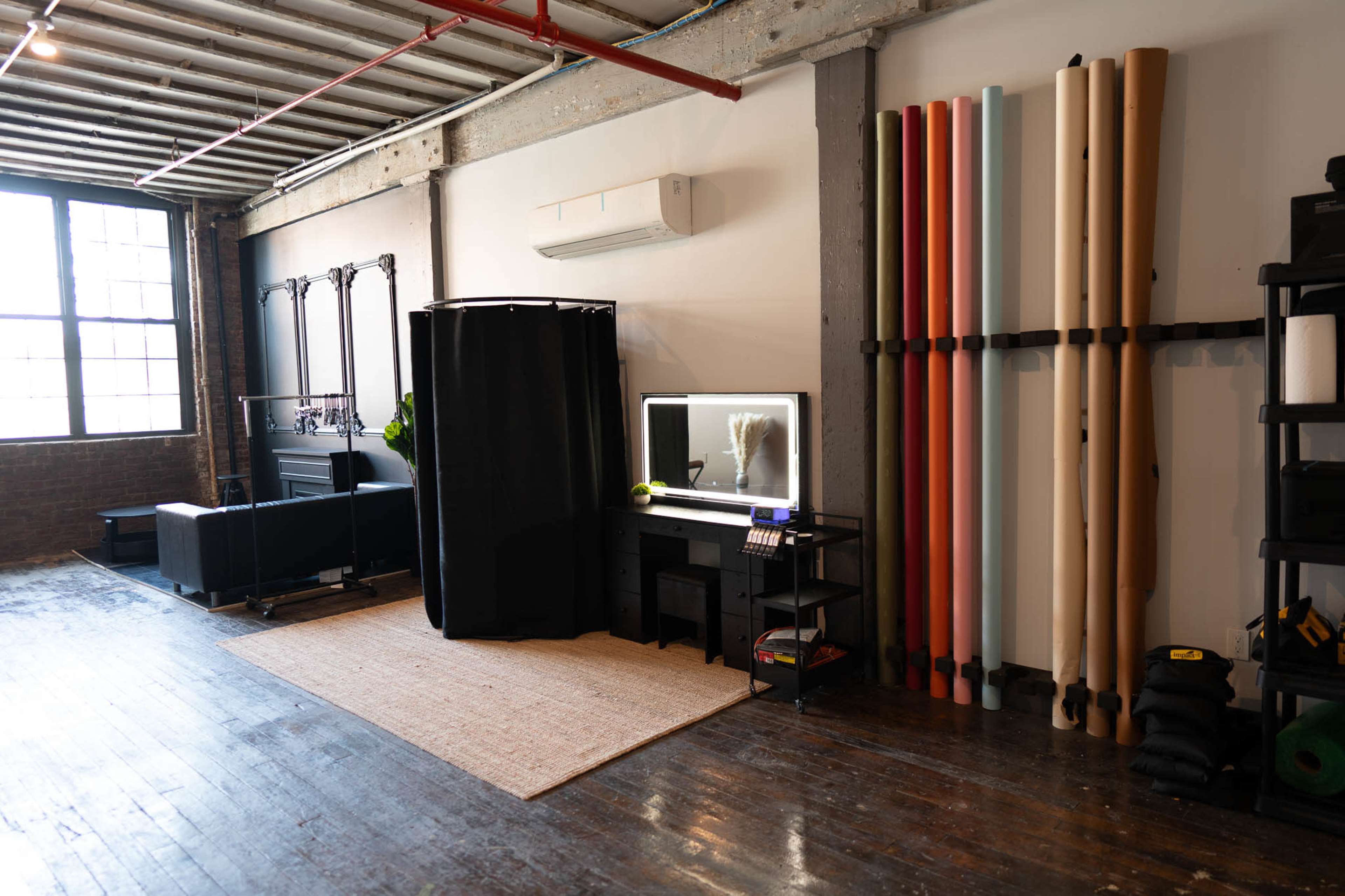 A spacious interior with a decorative rug, a black curtain concealing a mirror, and rolls of colored paper neatly arranged against the wall.