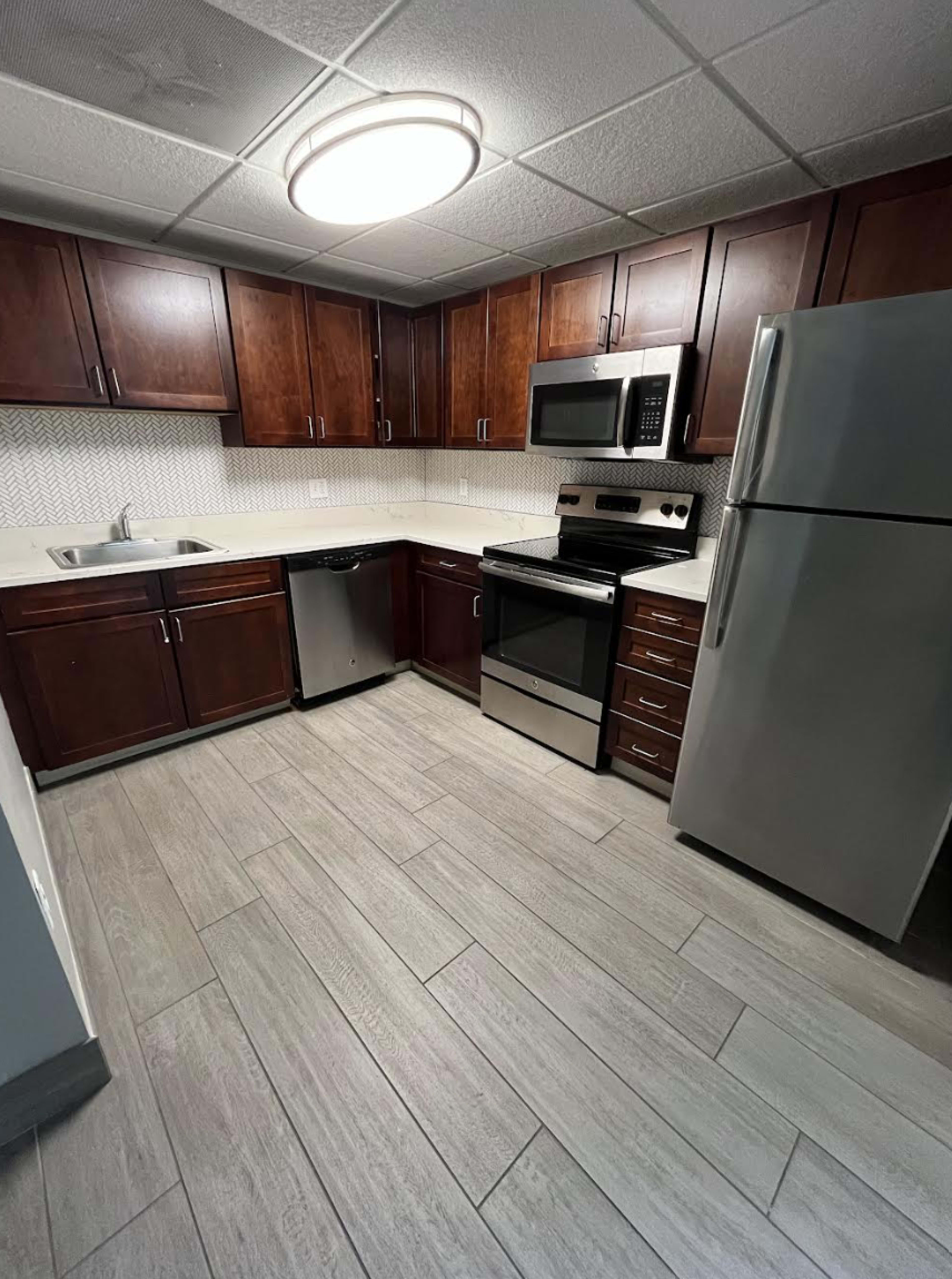 The image shows a modern kitchen featuring dark wood cabinets, stainless steel appliances, and a light-colored countertop.