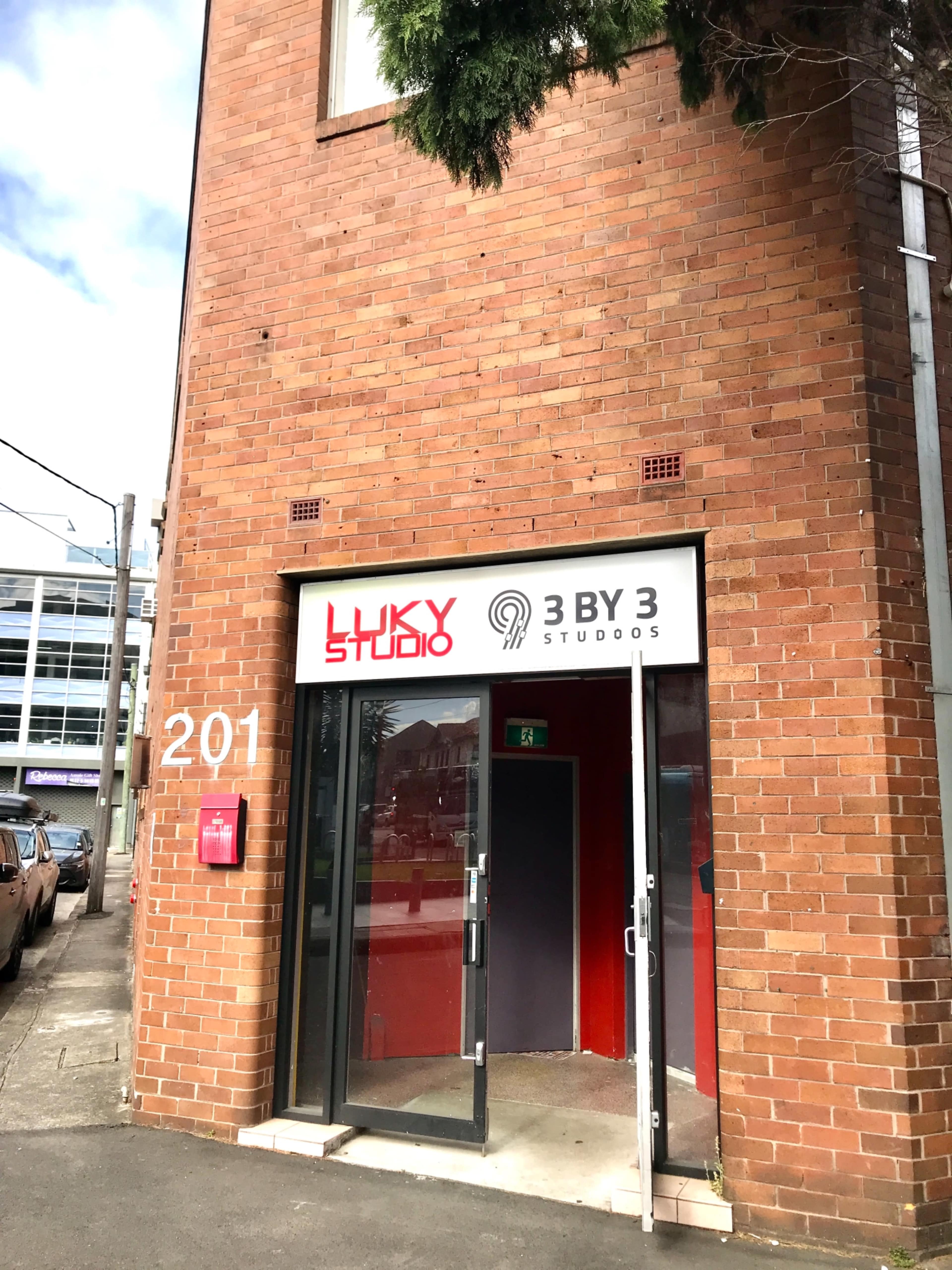 The entrance of a brick building at 201, featuring a sign for "LUXY STUDIO" and "3 BY 3 STUDIOS."