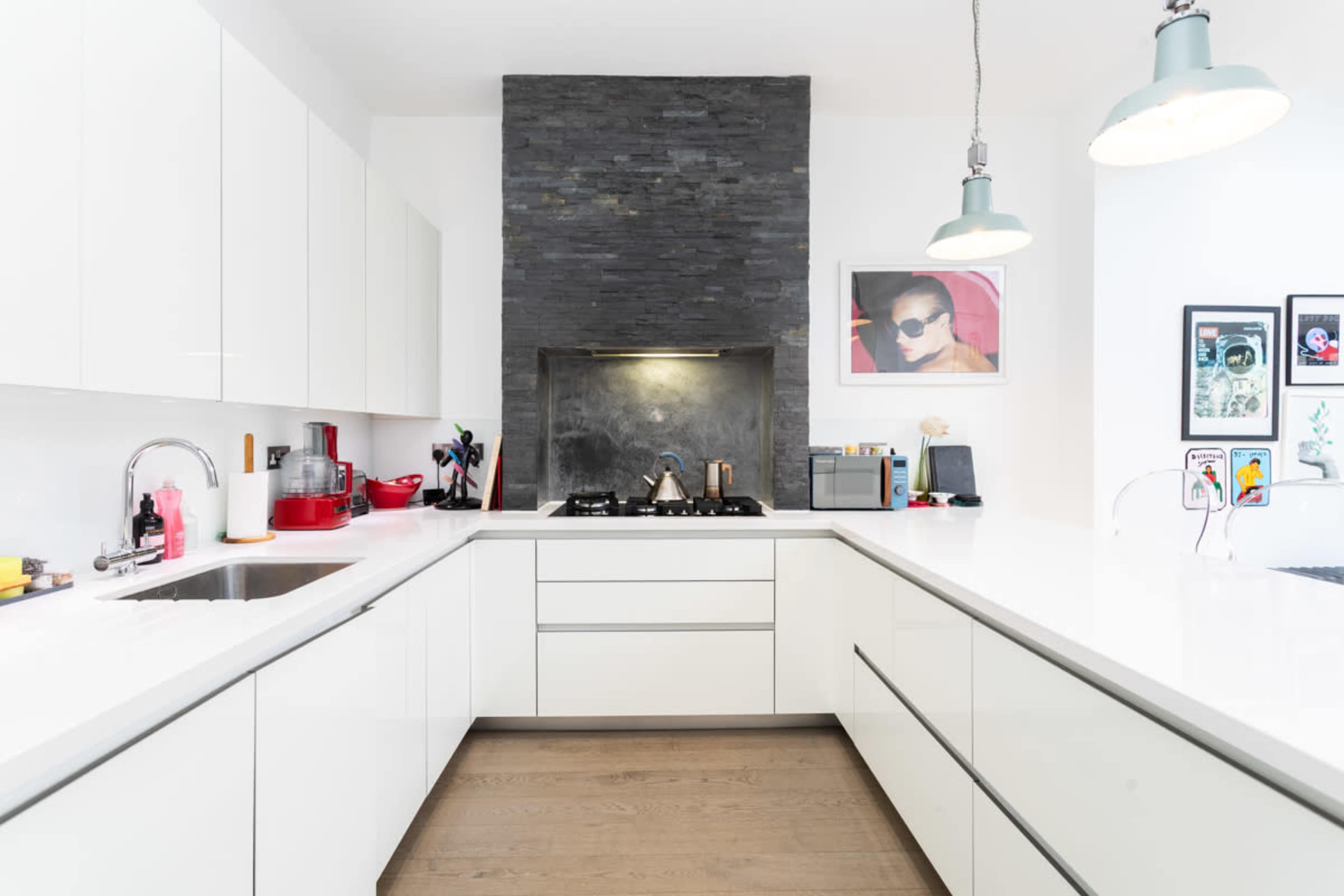 A modern kitchen features white cabinetry, a sleek countertop, and a dark stone backsplash with a stove and various kitchen appliances.