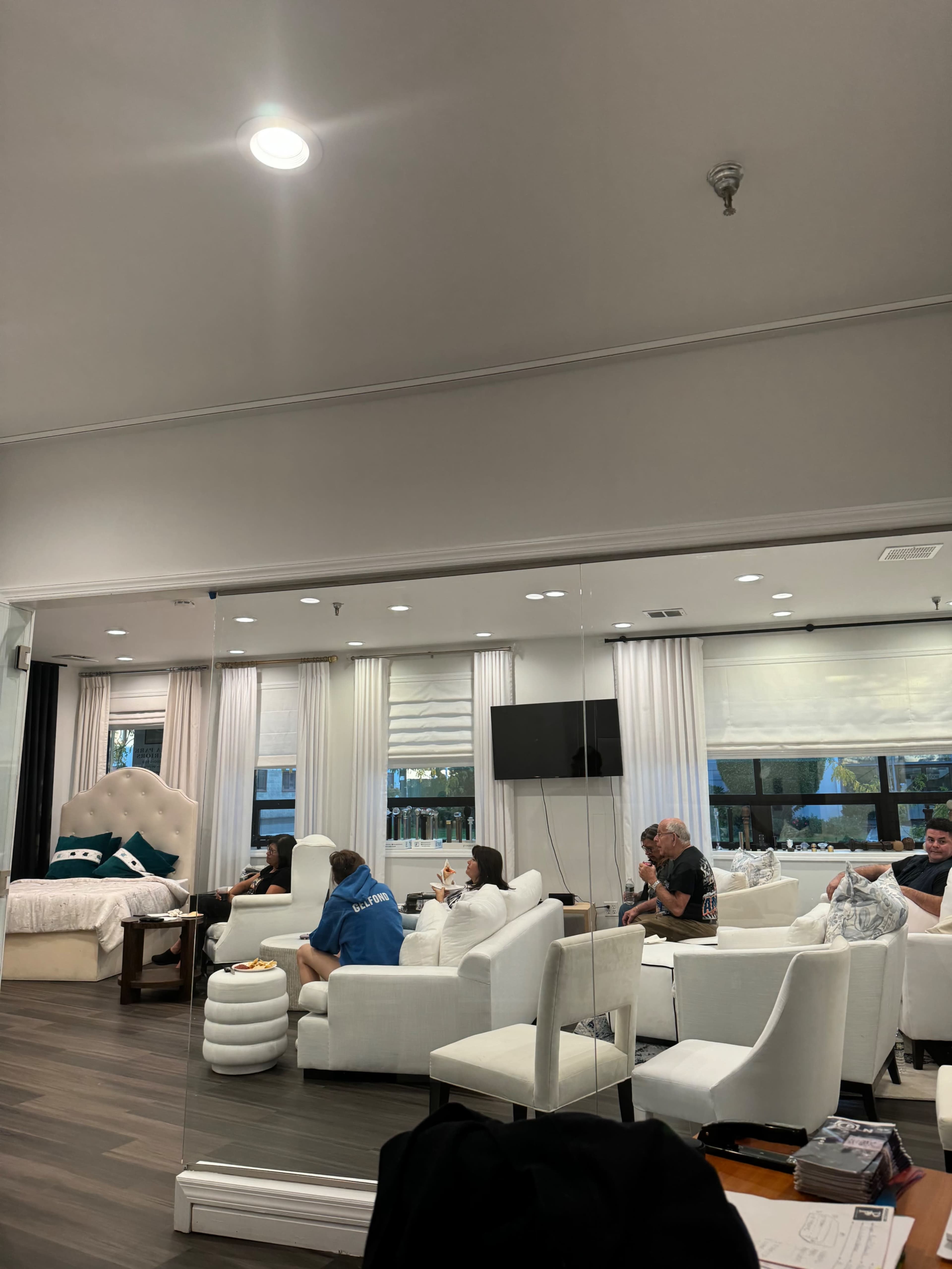 A group of people sits in a modern living room with white furniture and large windows.