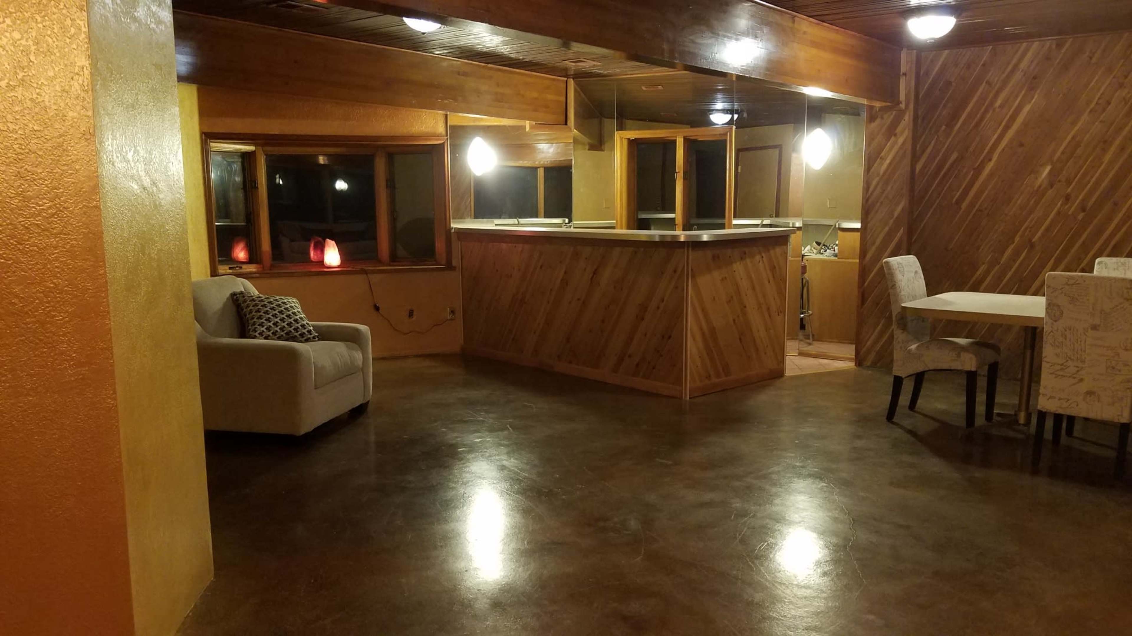 A room with a concrete floor, a kitchen bar area, light fixtures, and a seating area with a sofa and dining table.