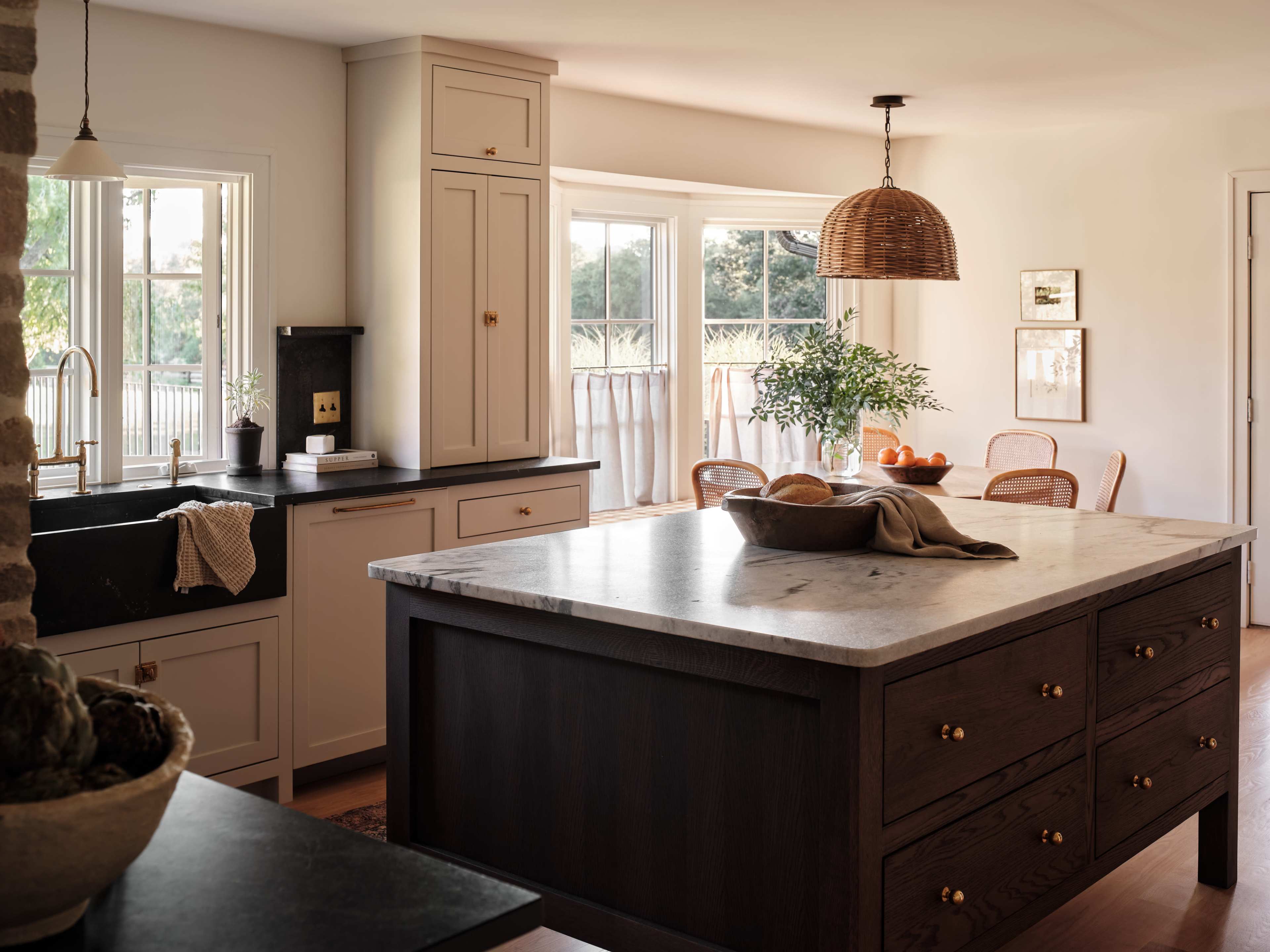 A spacious kitchen features a large marble island with dark wood drawers, complemented by a sink and windows that provide natural light.