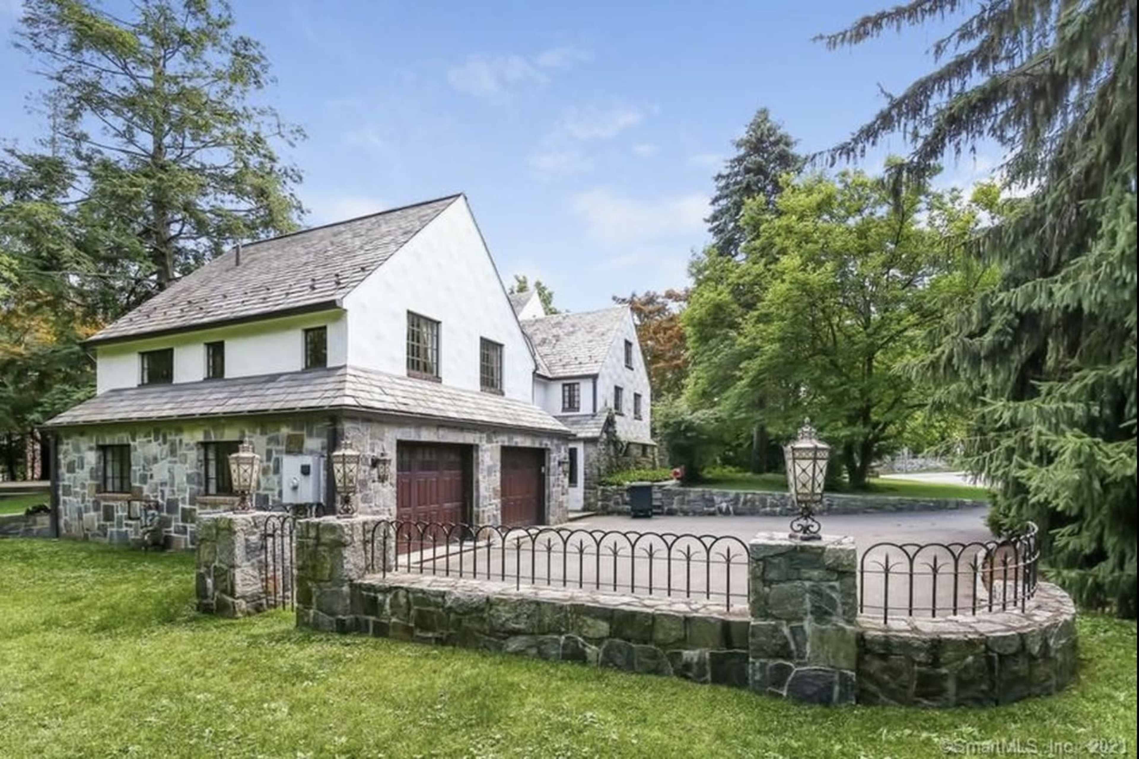 A large, two-story house with a stone exterior and a gabled roof, set on a grassy area surrounded by trees.