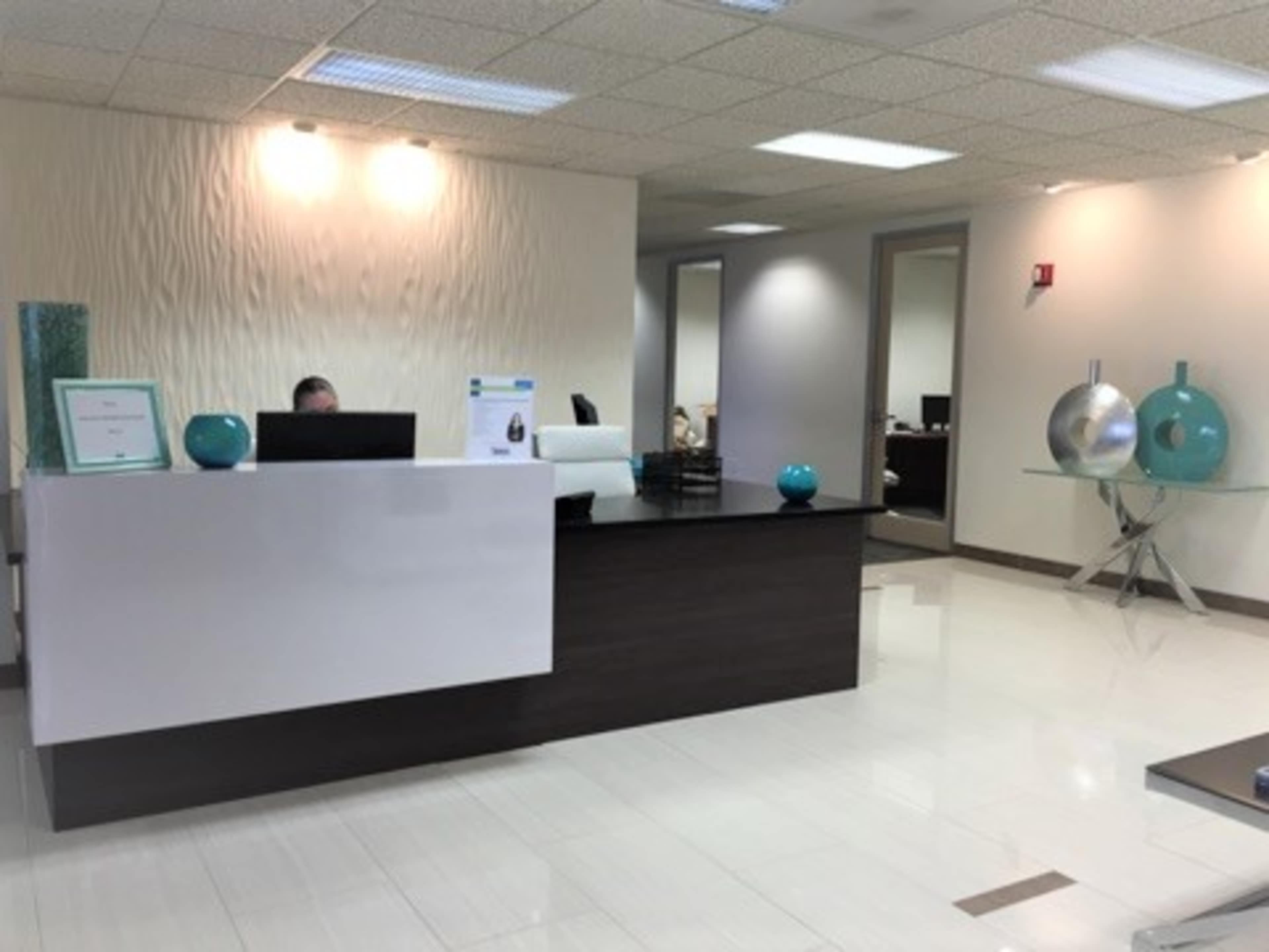 A modern office reception area with a sleek white desk, a dark wooden counter, and decorative turquoise objects on display.