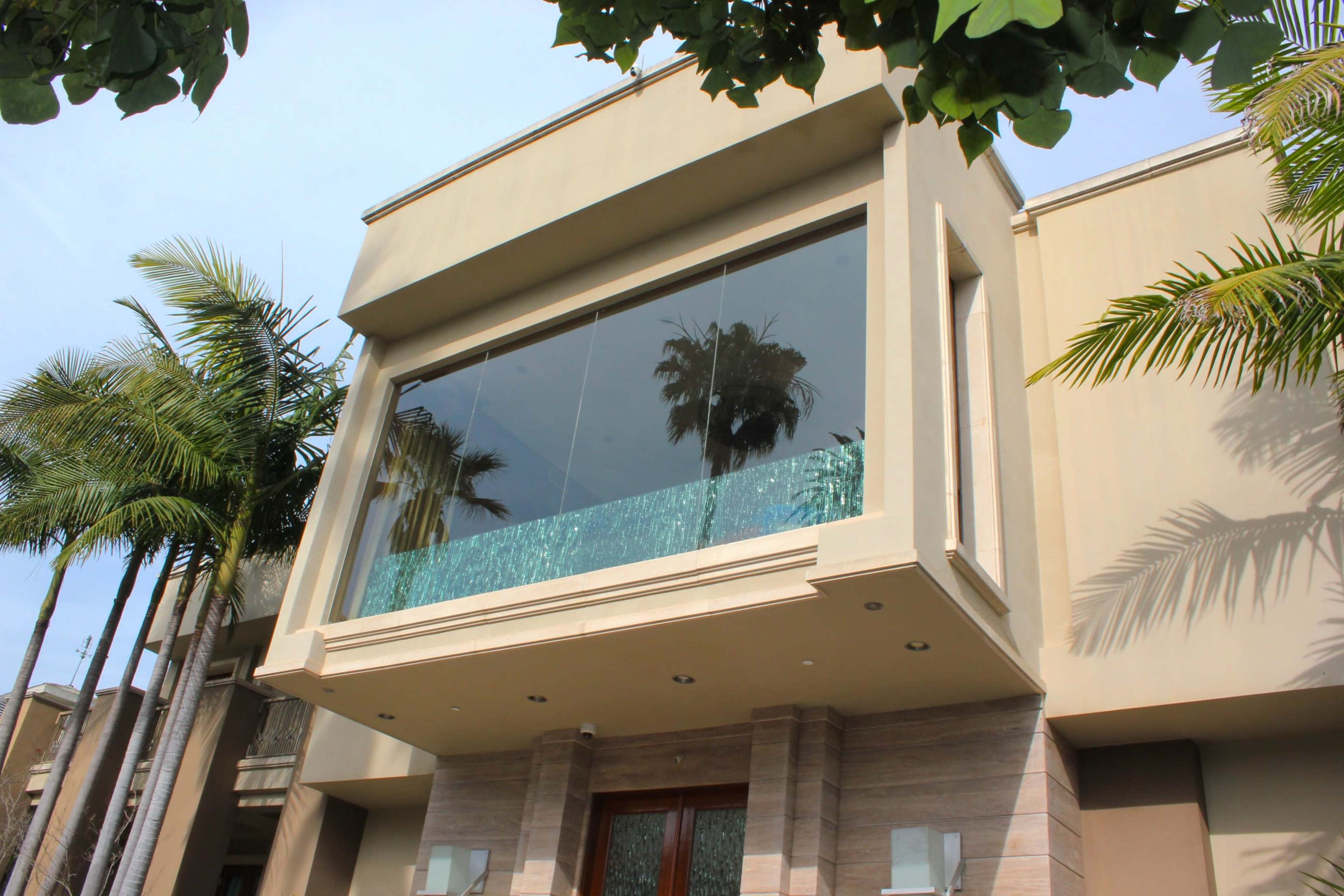 The image shows a modern building with a large glass balcony, flanked by palm trees.