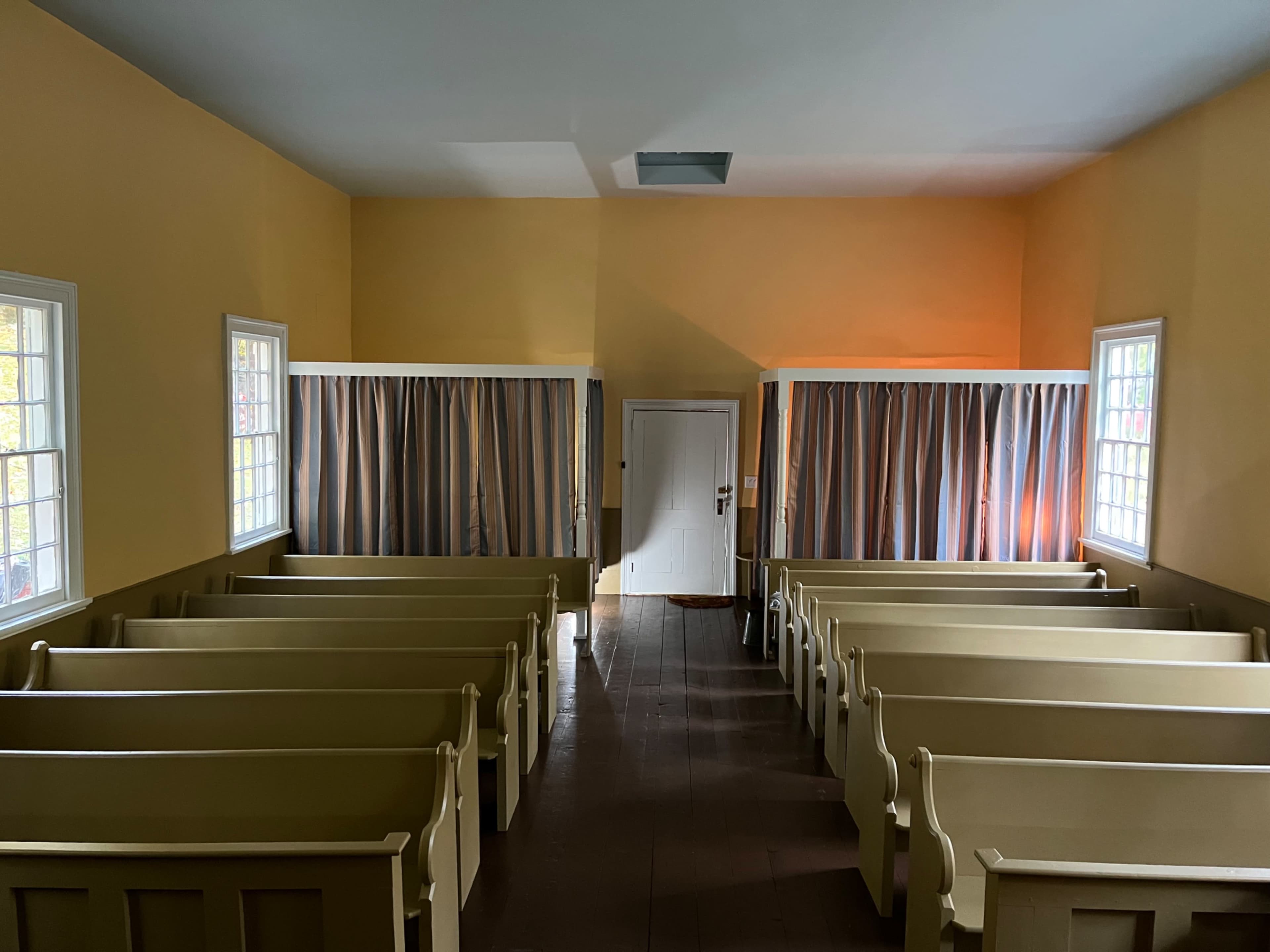 The image shows an interior of a small church with rows of wooden pews and curtains dividing sections on either side.