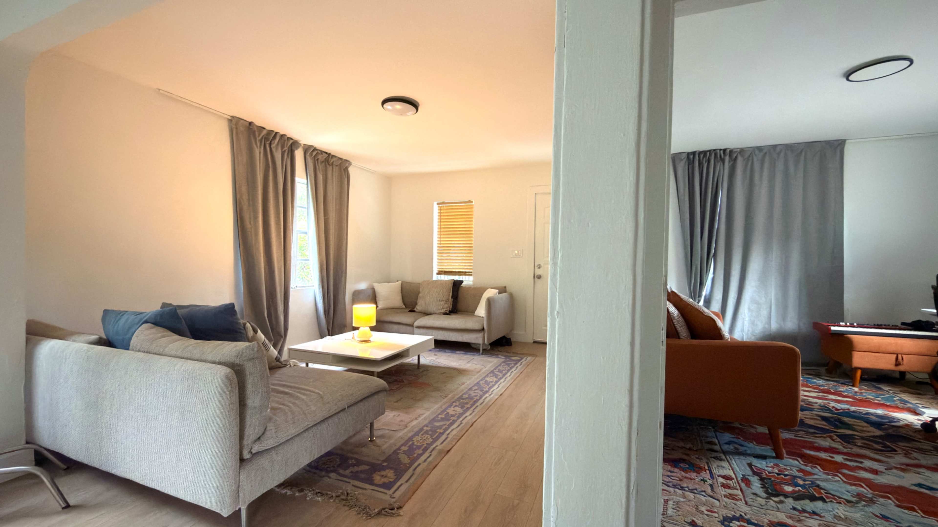 The image depicts a bright living room with two seating areas, a coffee table, and natural light streaming through the windows.