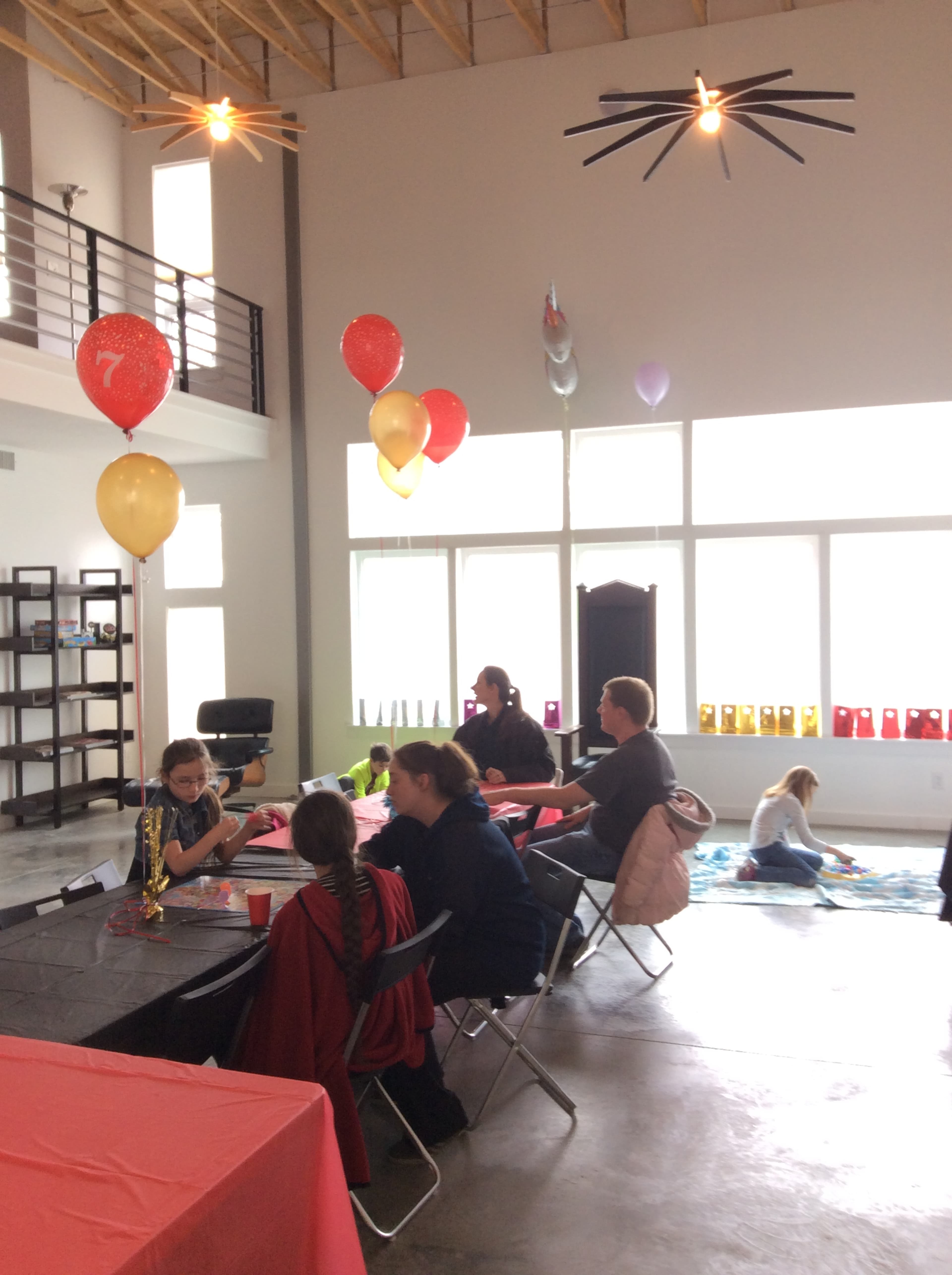 A birthday party is taking place in a spacious, well-lit room with balloons and tables set up for guests.