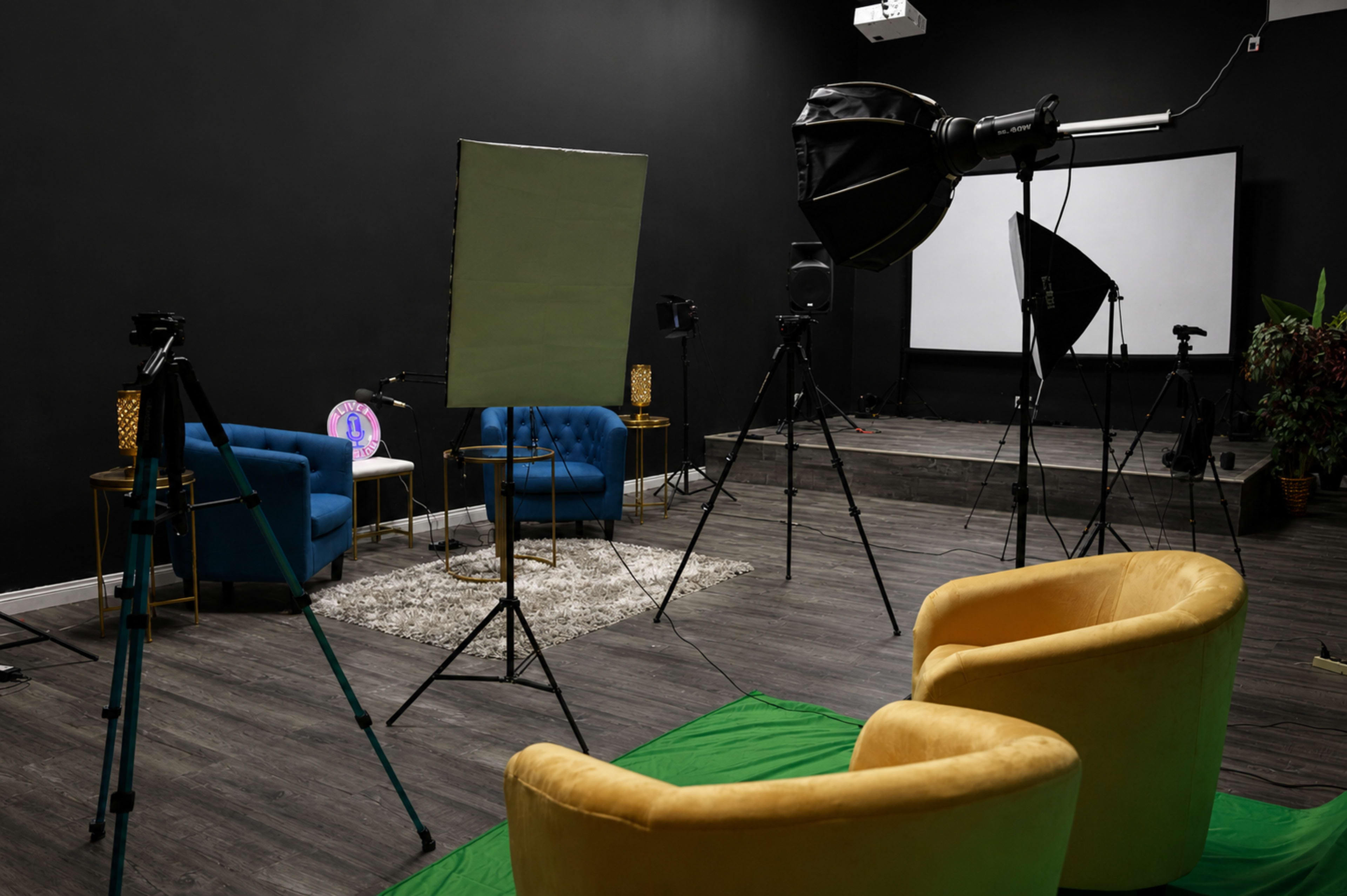 The image shows a photography studio with two blue chairs, two yellow chairs, various lighting equipment, and a backdrop setup.
