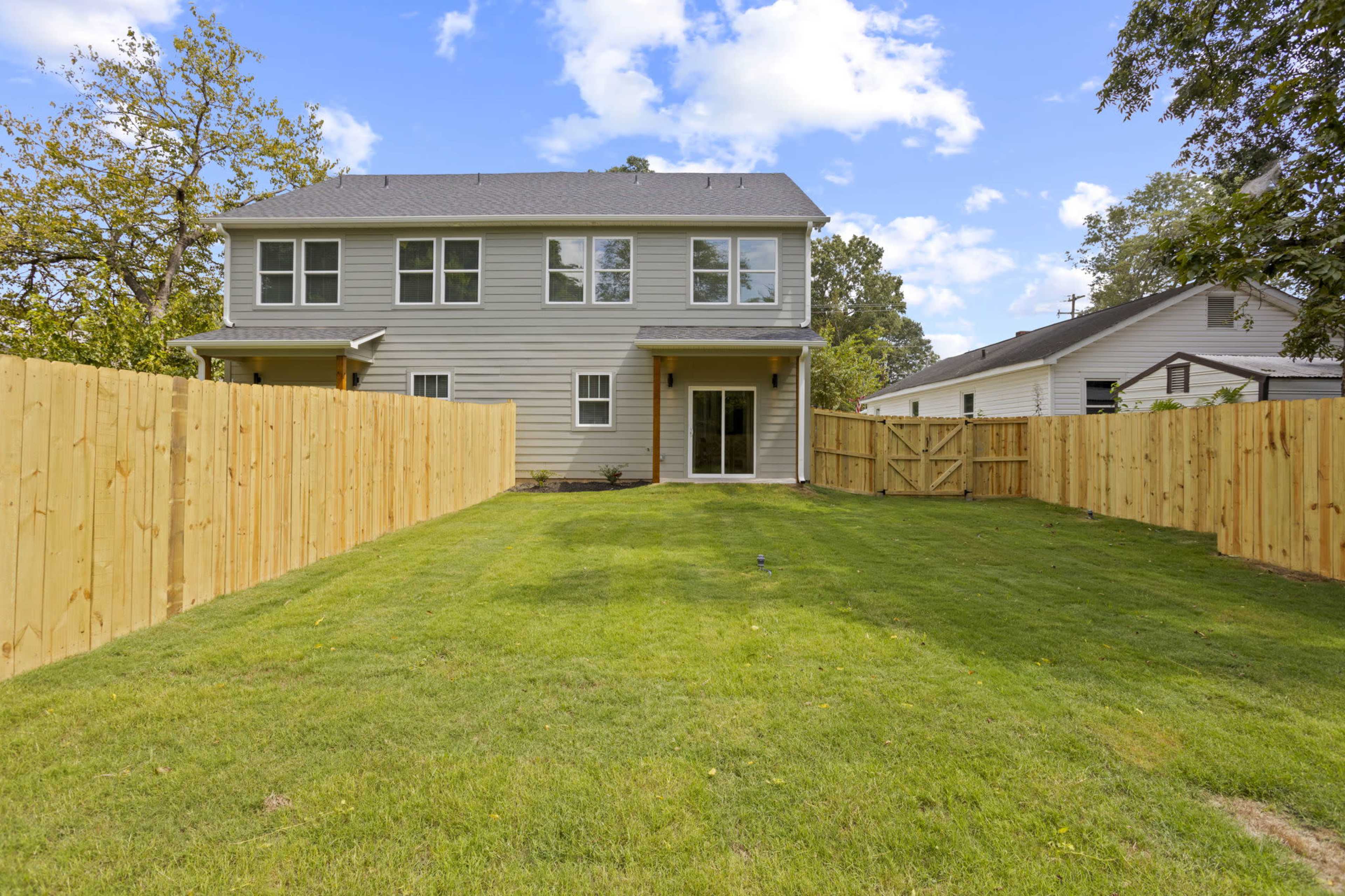 The image shows a two-story residential house surrounded by a newly constructed wooden fence and a well-maintained grassy yard.