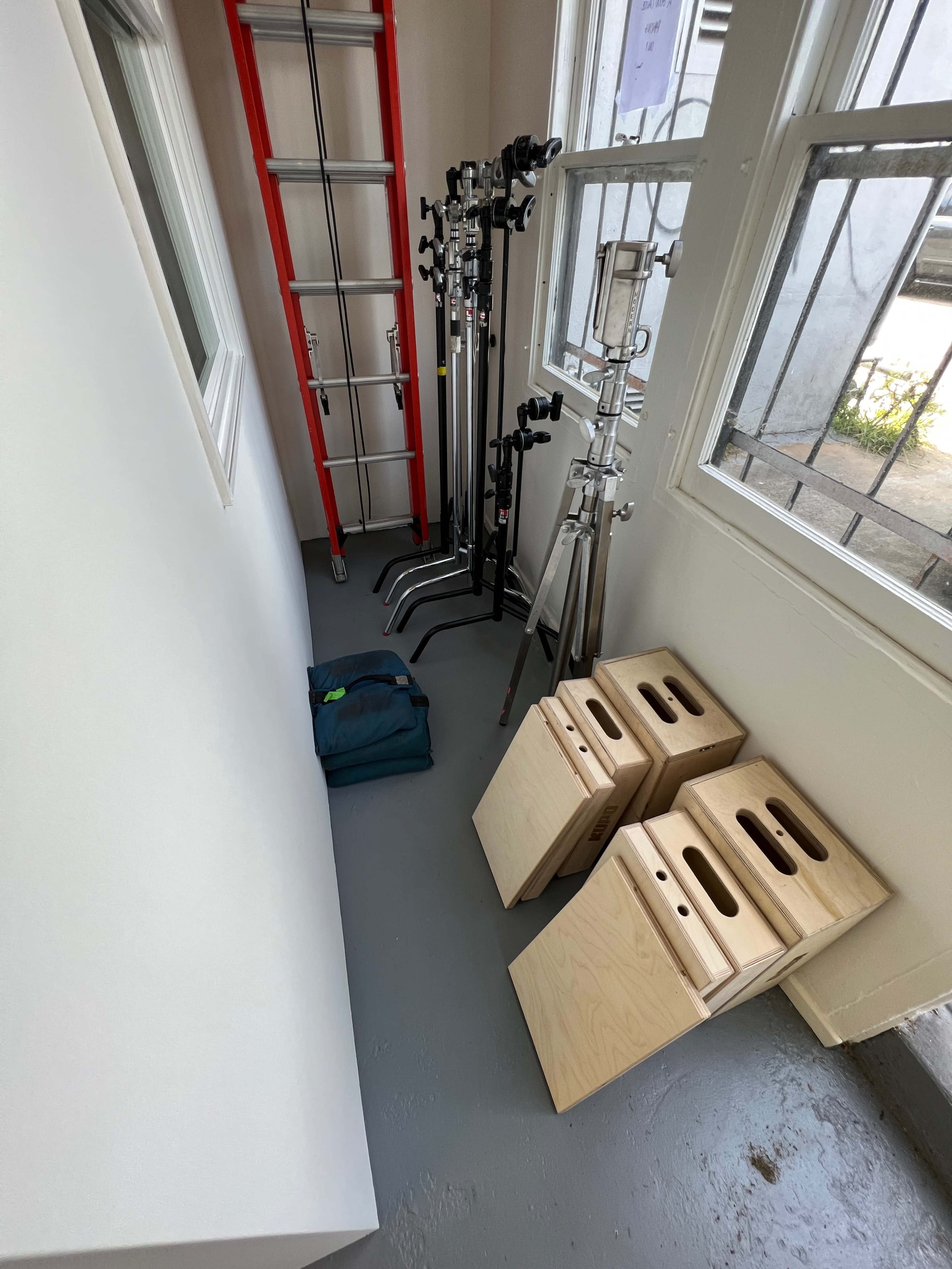 A narrow room with photography equipment including light stands, a ladder, and wooden boards on the floor.