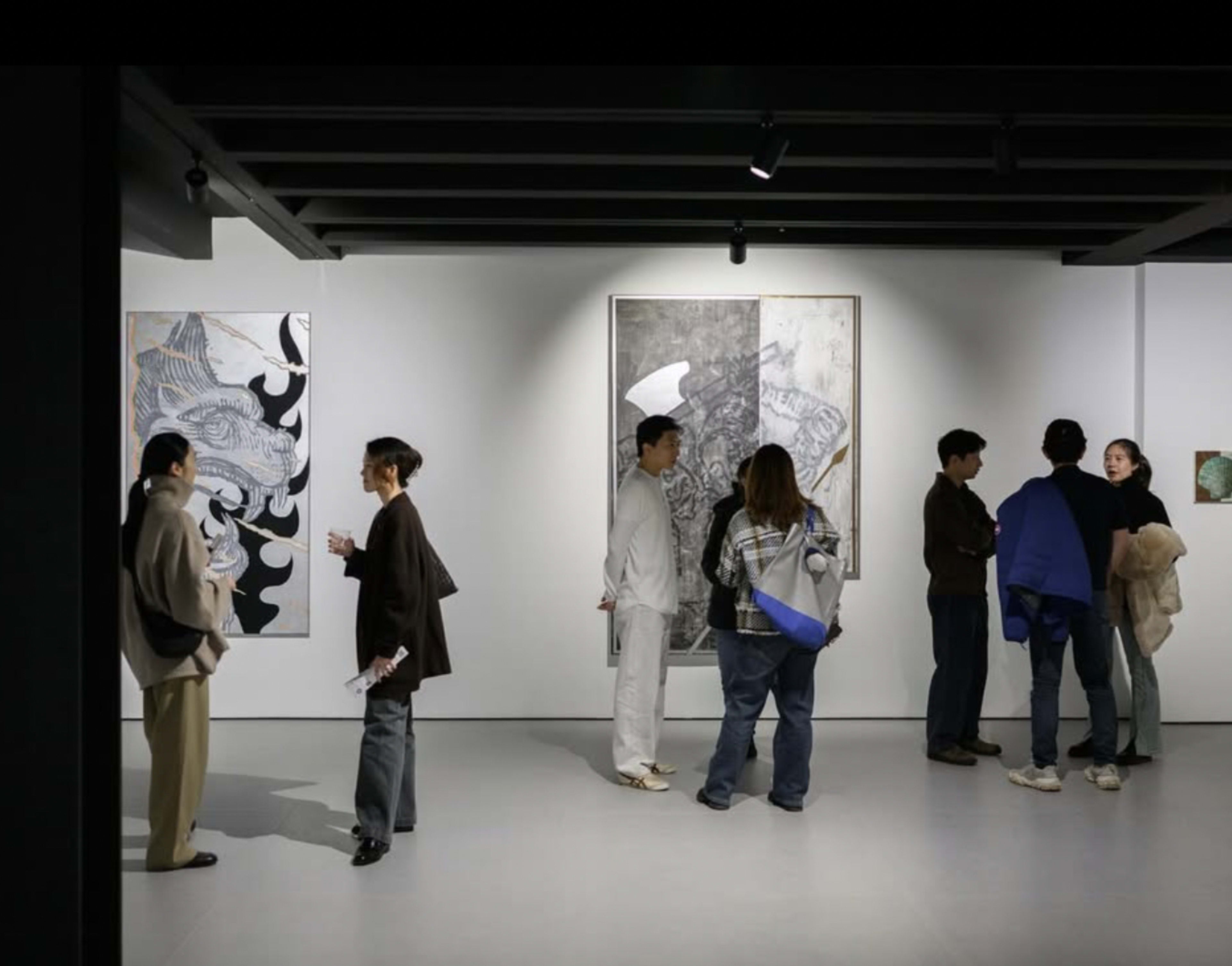 A group of people is engaged in conversation in an art gallery featuring several large artworks on the walls.