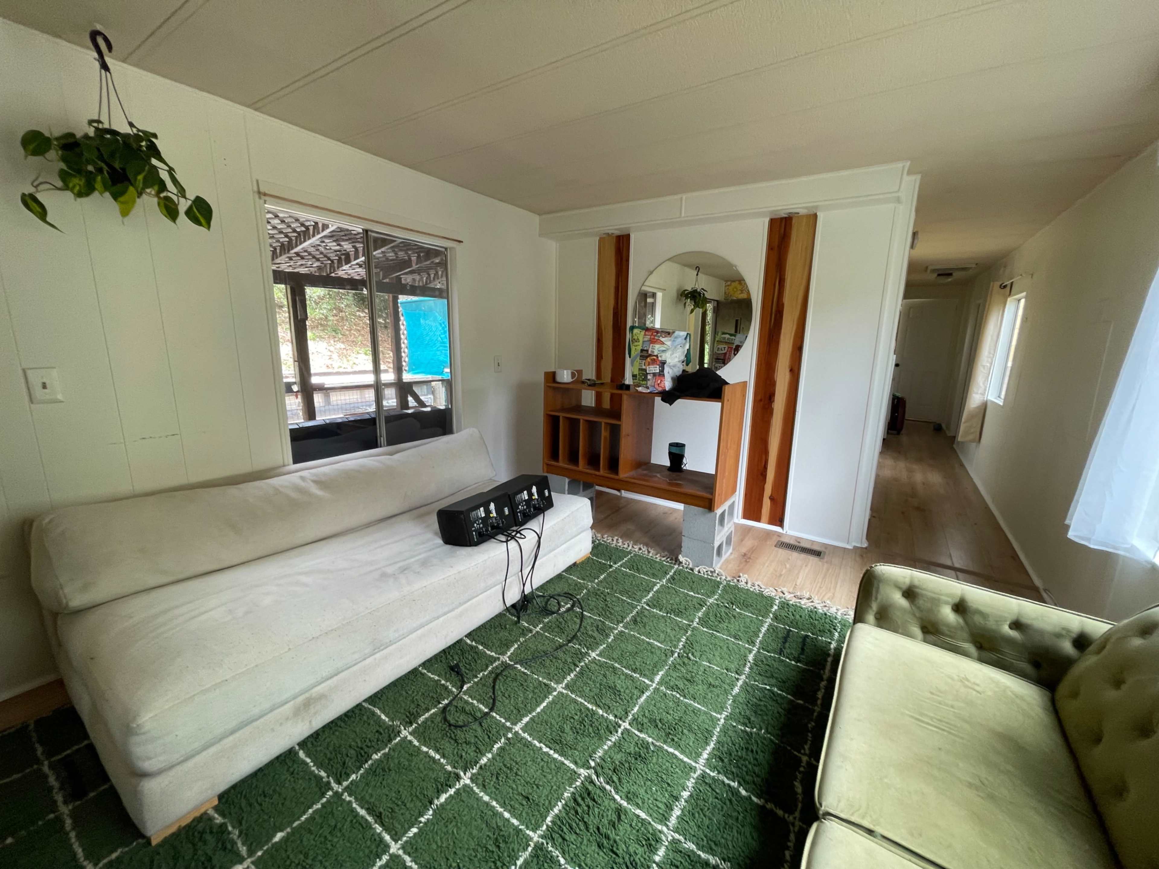 The image shows a living room with a white couch, a green patterned rug, and a wooden console table with a round mirror on the wall.