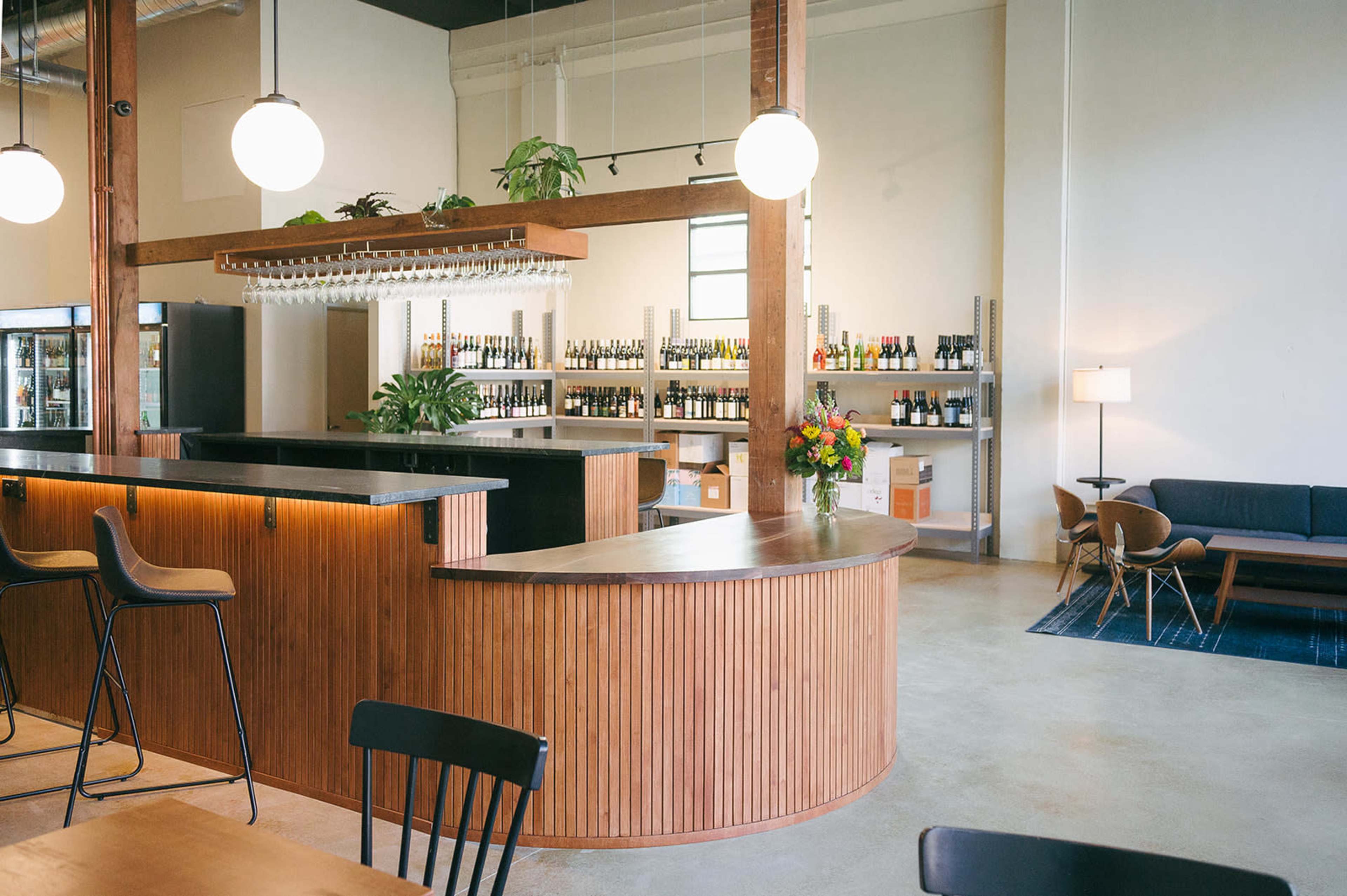 The image shows a modern, stylish bar area with wooden accents, shelves filled with bottles, and seating for guests.