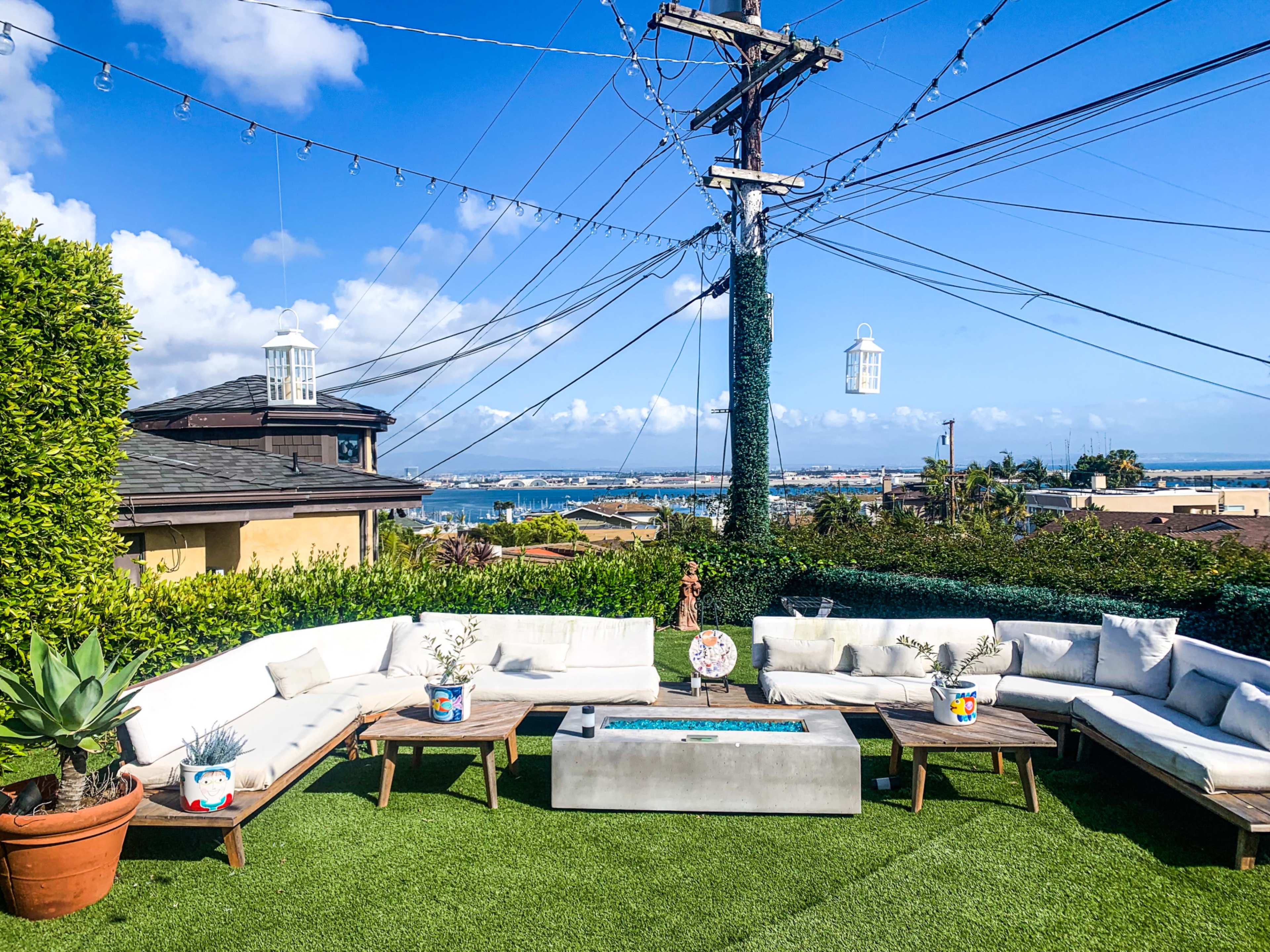 A modern outdoor seating area features a sectional sofa, a rectangular coffee table, and a scenic view of a coastal landscape under a blue sky with scattered clouds.