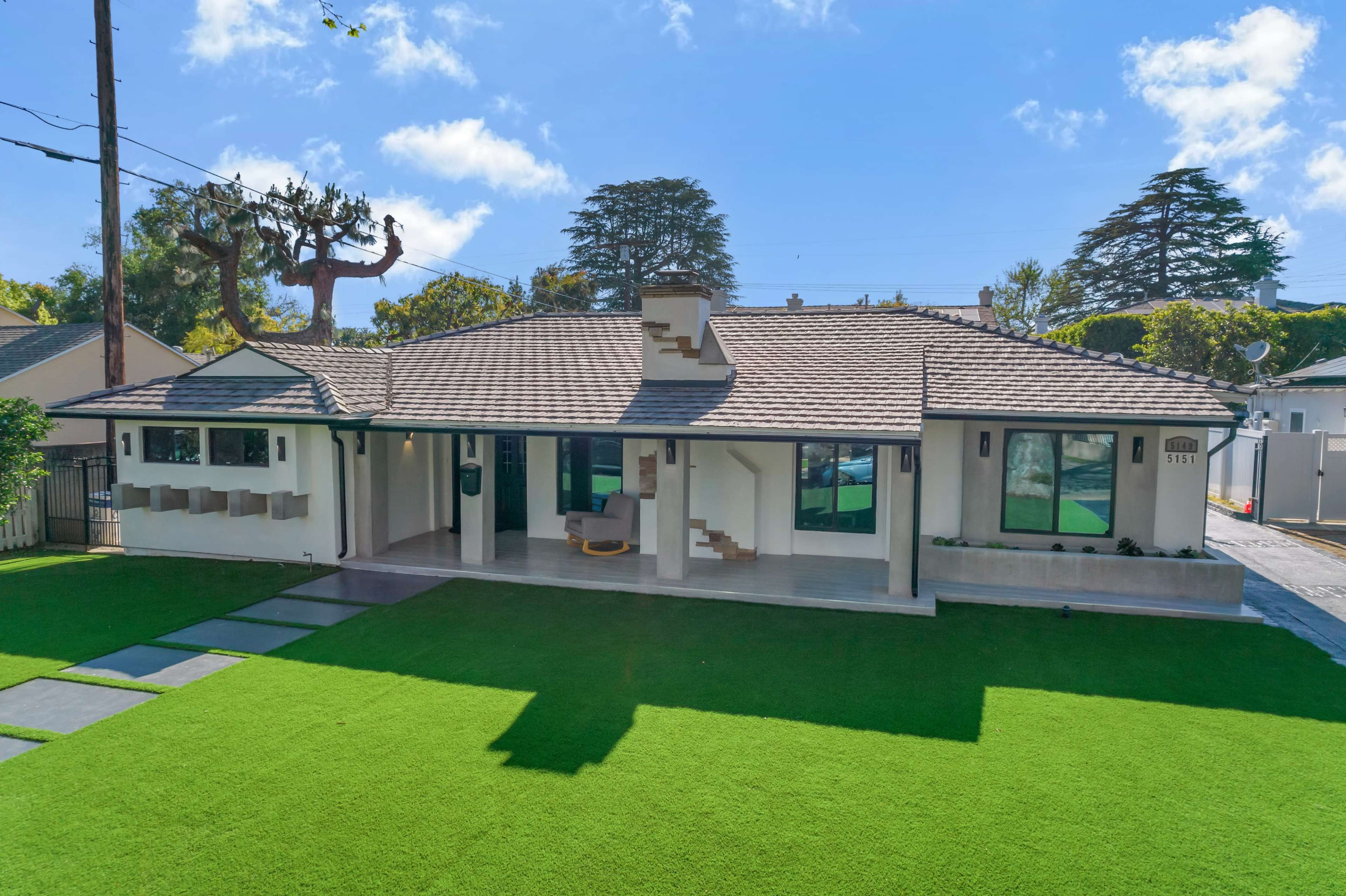 A modern single-story house with a sloped roof is set on a landscaped yard featuring artificial grass and stone pathway.